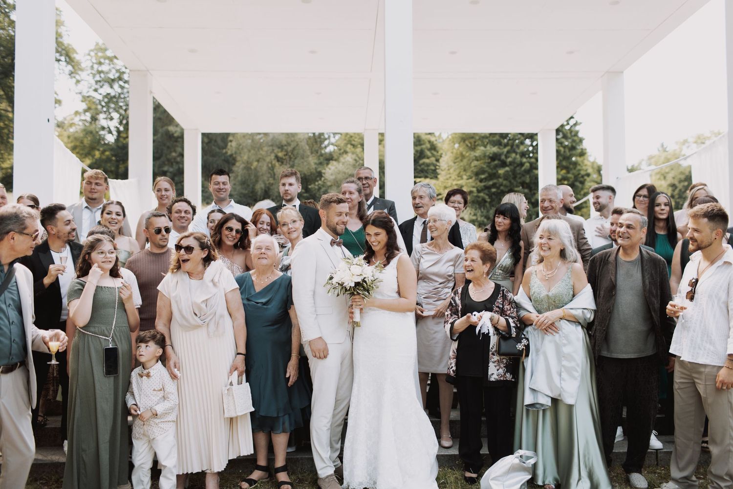 Wedding party members gather together in formal attire for group photos outside a white building.