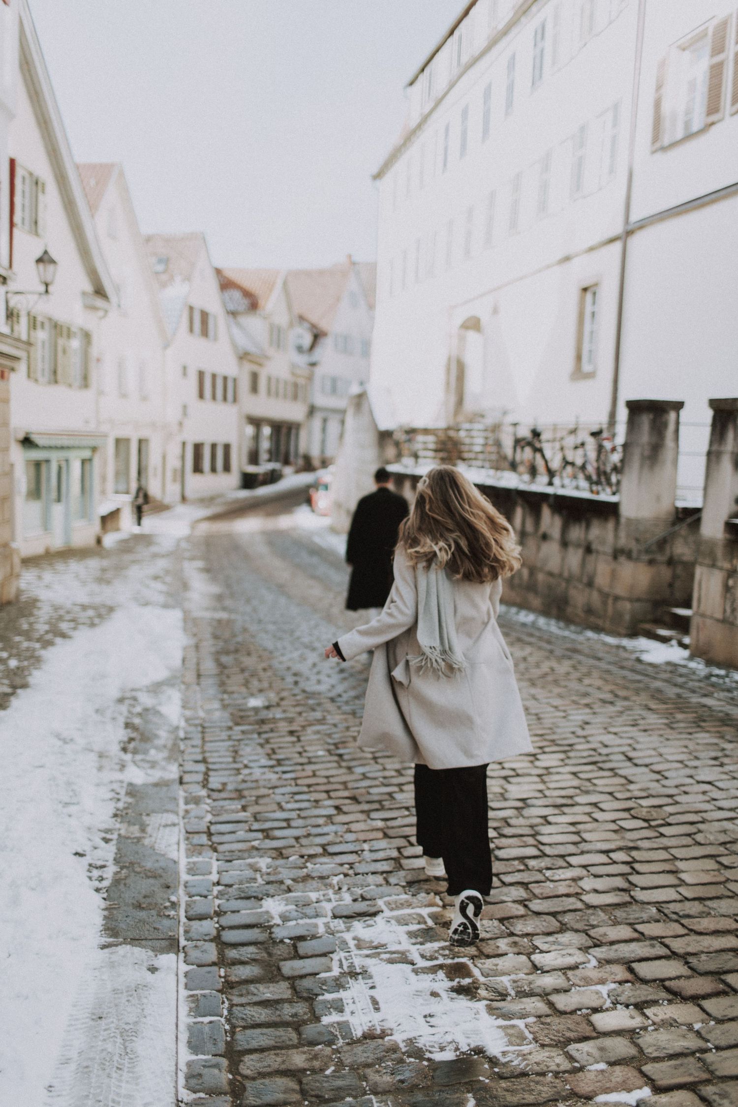A person walking down a cobblestone street in a European town on a winter day.