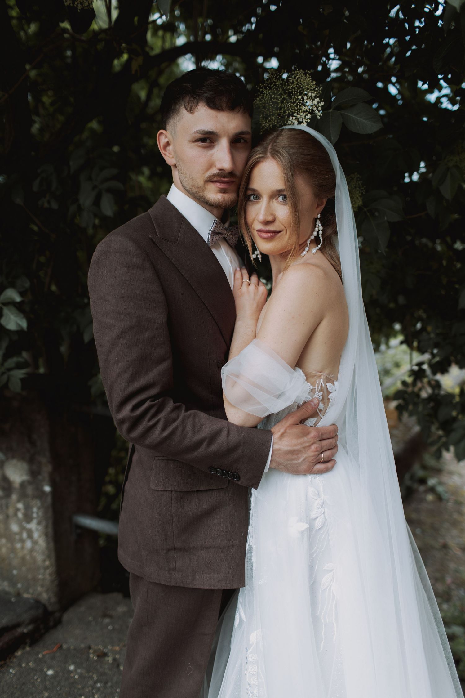 An intimate wedding portrait of a couple embracing against a lush garden backdrop.
