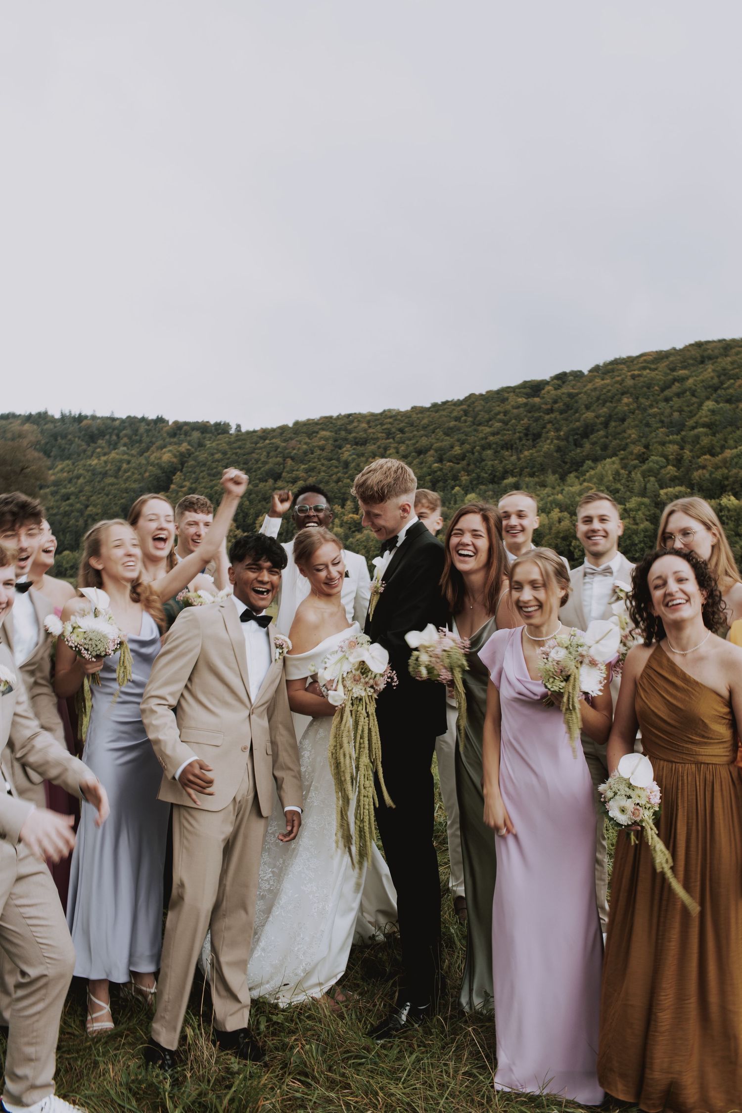 Wedding party group photo with bridesmaids in pastel dresses against mountain backdrop.