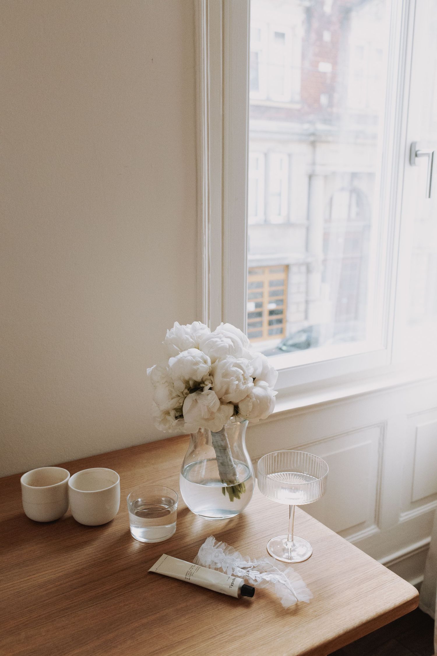 Minimalist table setting with white flowers in vase near bright window.