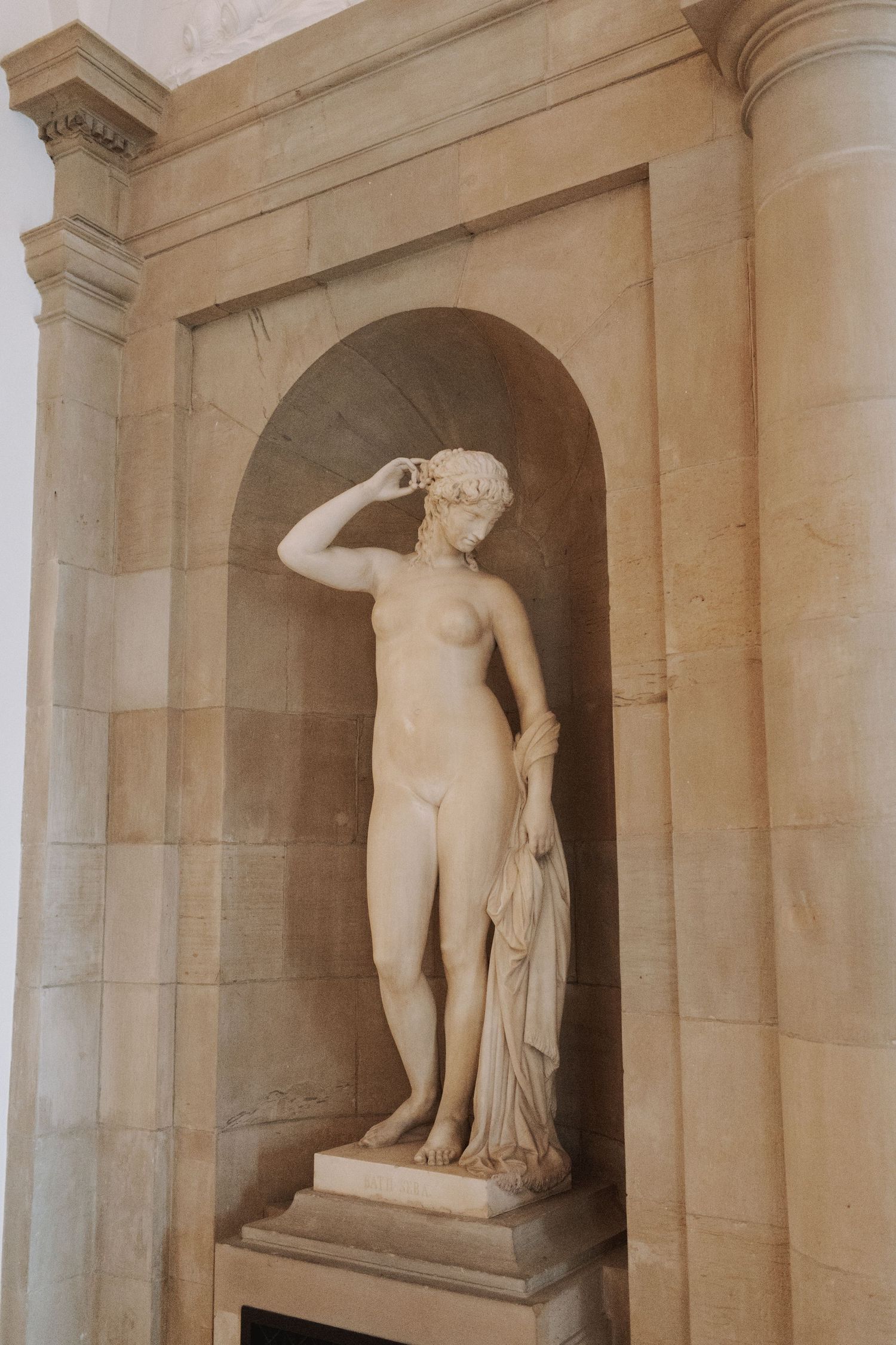 Classical nude statue in stone alcove with architectural details.
