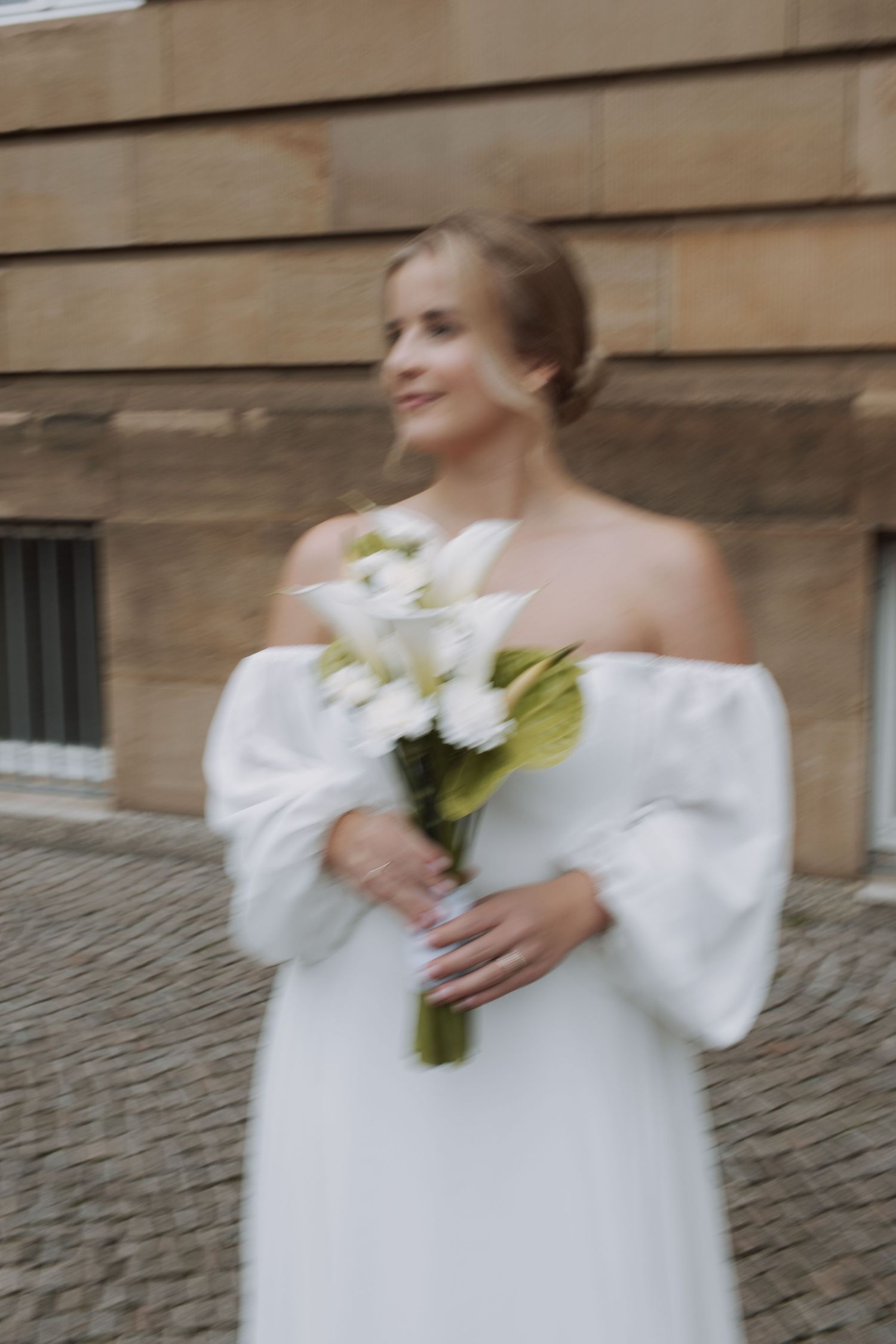 Bride in an off-shoulder wedding dress holds a white lily bouquet.