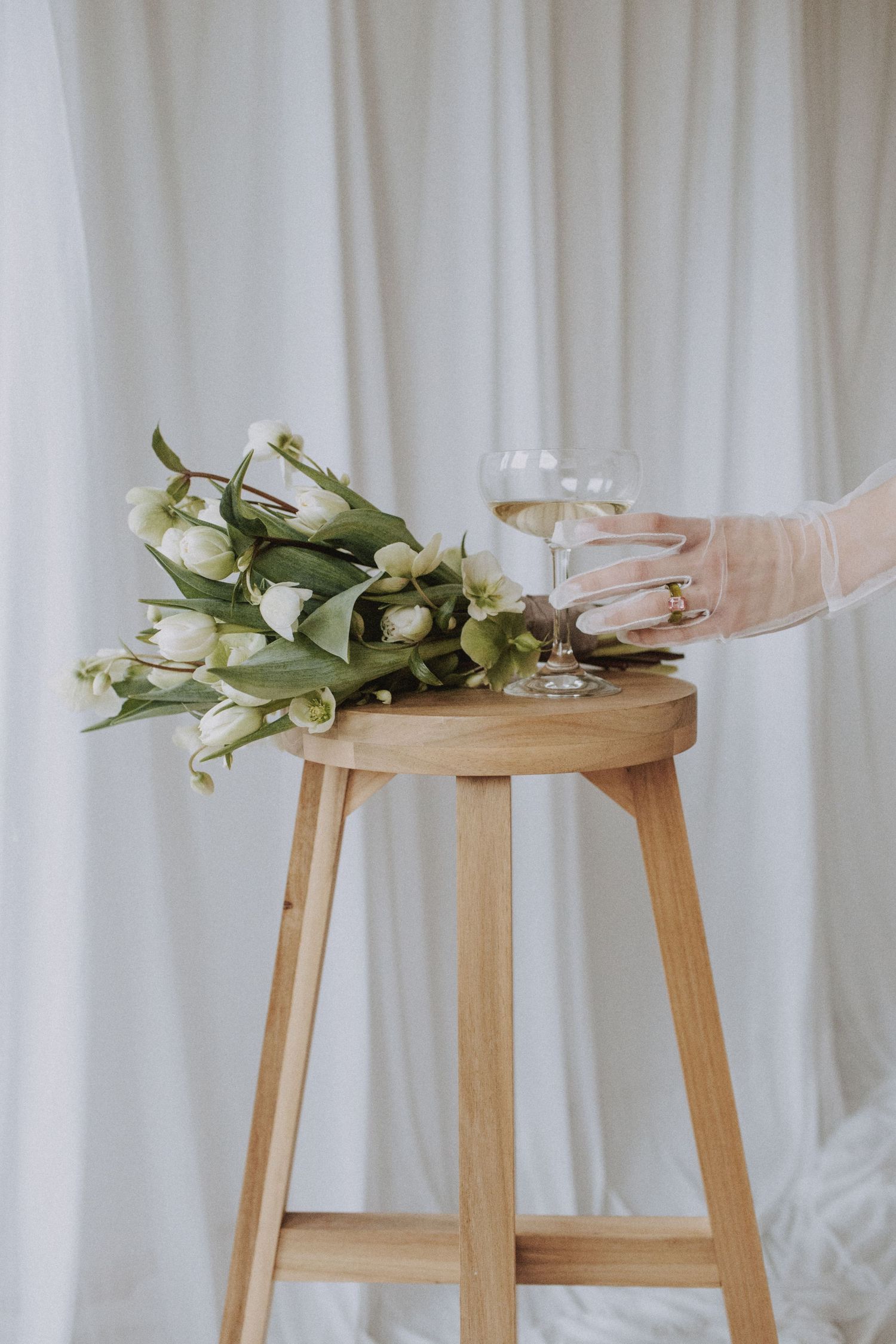 Wooden stool with white roses and delicate wedding accessories against white backdrop.