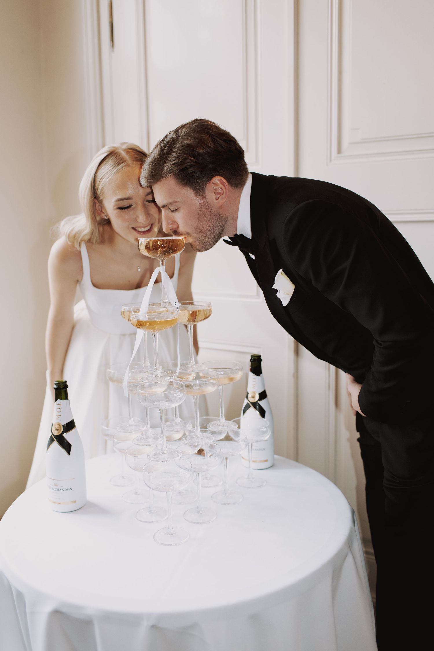 Couple leaning over a white table with glasses during an intimate wedding moment.