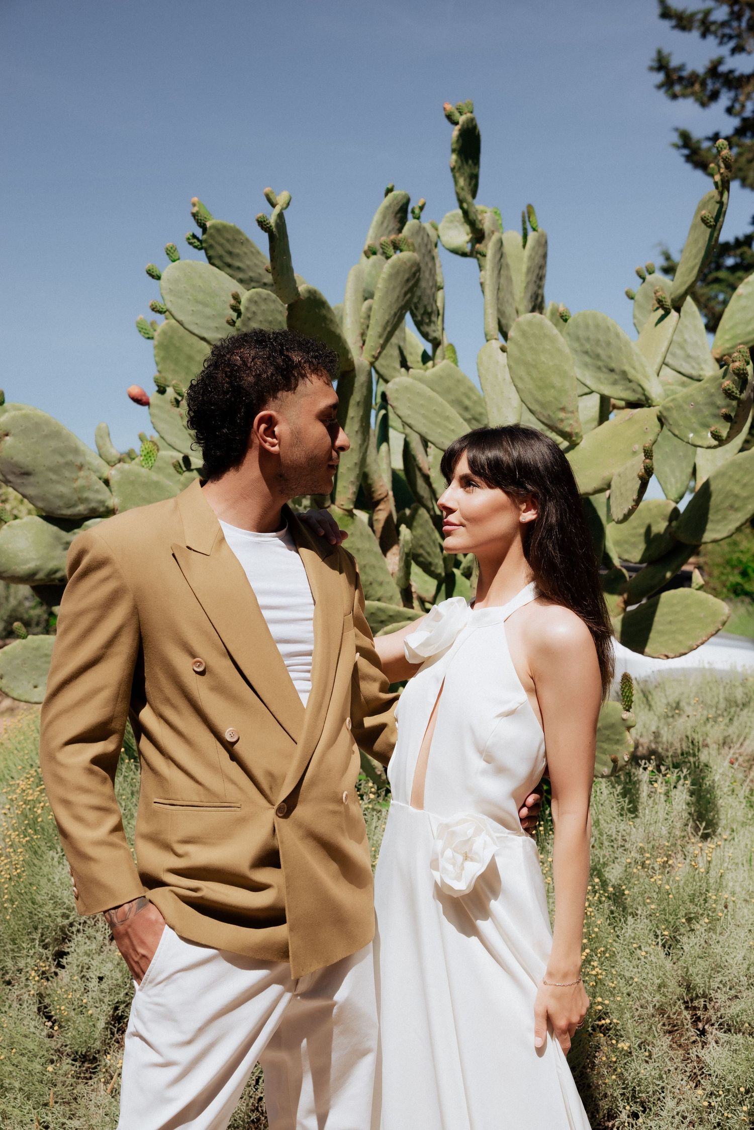 Bride and groom walking together through a sunlit garden, surrounded by trees and relaxed countryside vibes.