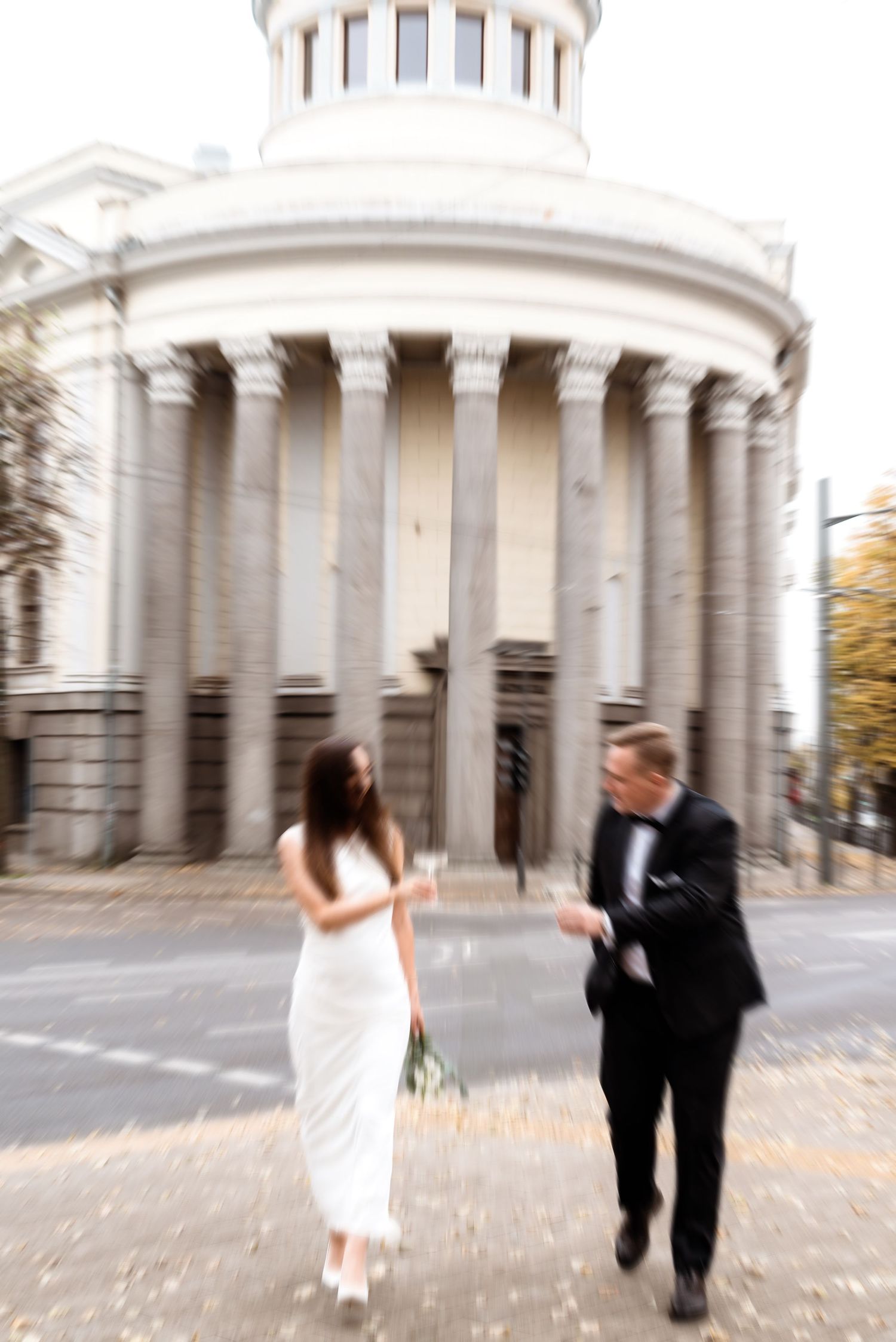 Bride and groom walking toward a classical stone rotunda, captured in soft natural light for an elegant editorial feel.