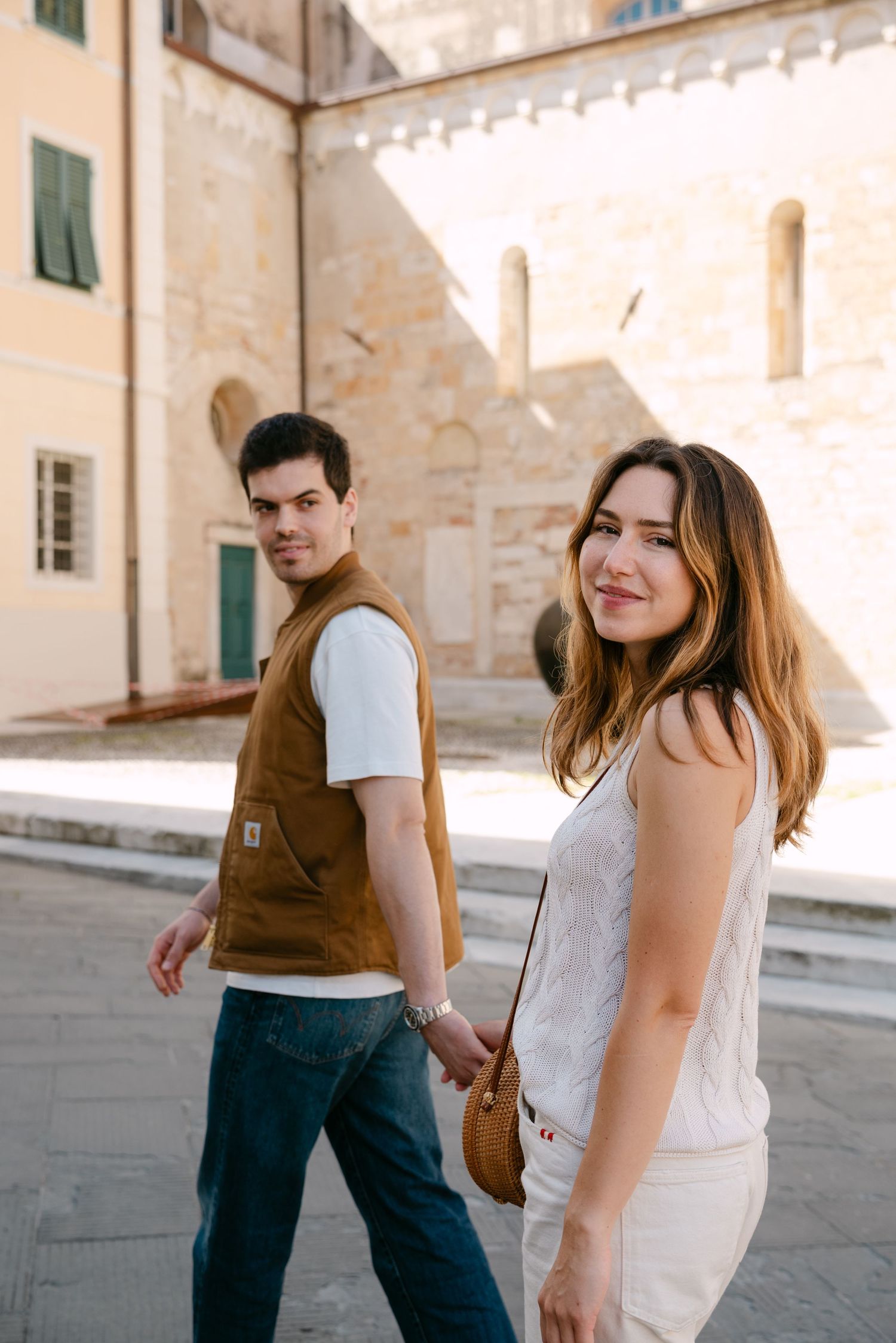 Bride and groom smiling as they walk together through a historic Italian town, hand in hand after their wedding ceremony.