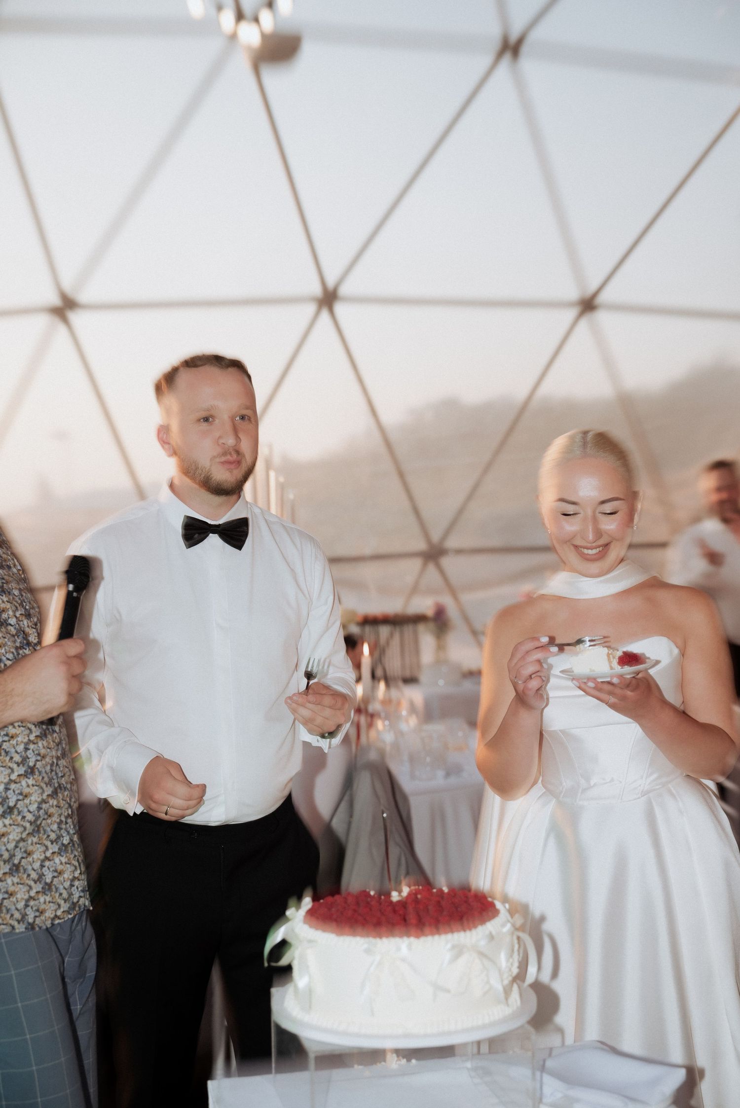 Groom smiling with a microphone during the wedding speech inside a tented reception, surrounded by guests in Lithuania, Klaipeda.
