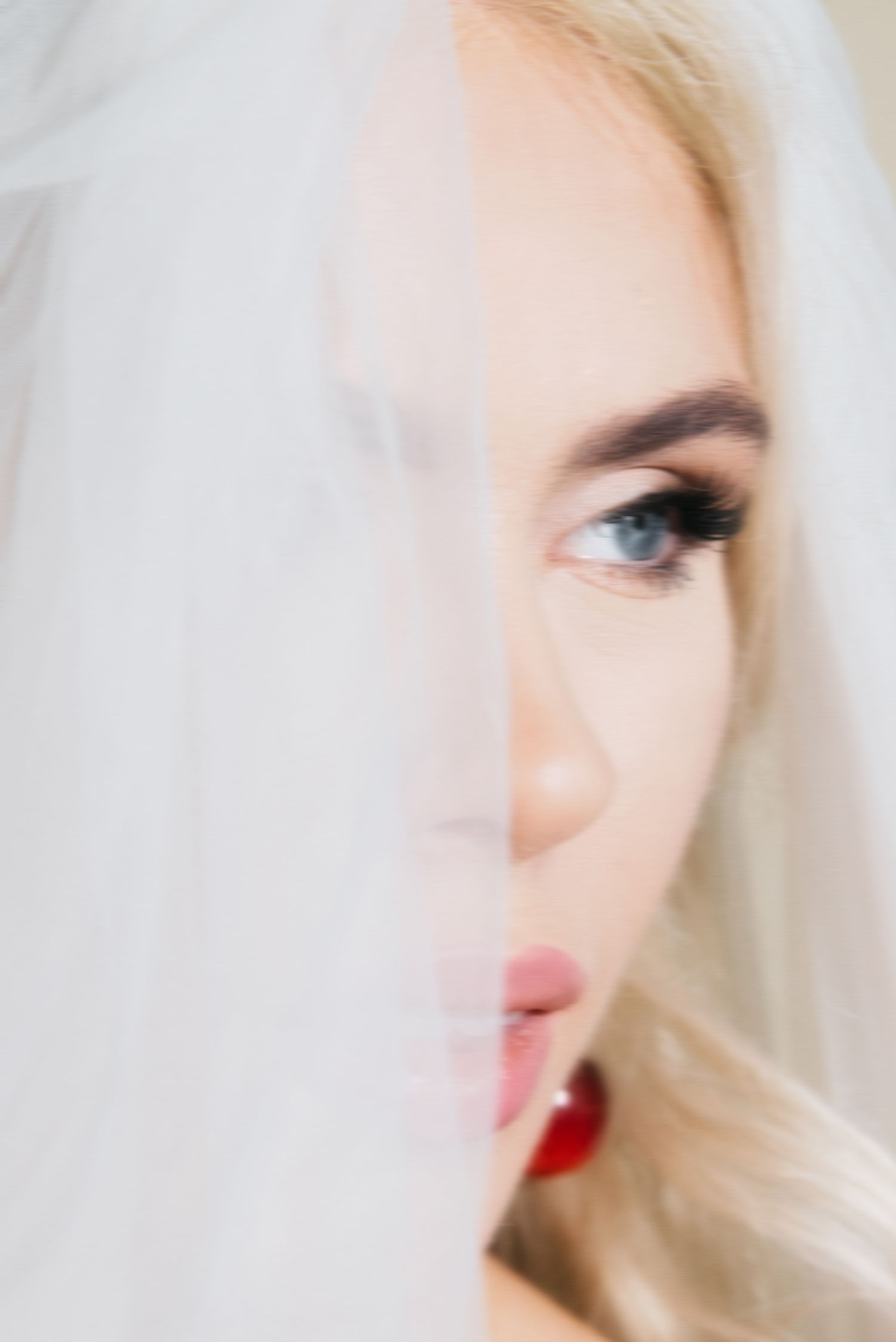 Close-up bridal portrait with soft focus — bride peeking through her veil, evoking a quiet, romantic moment.