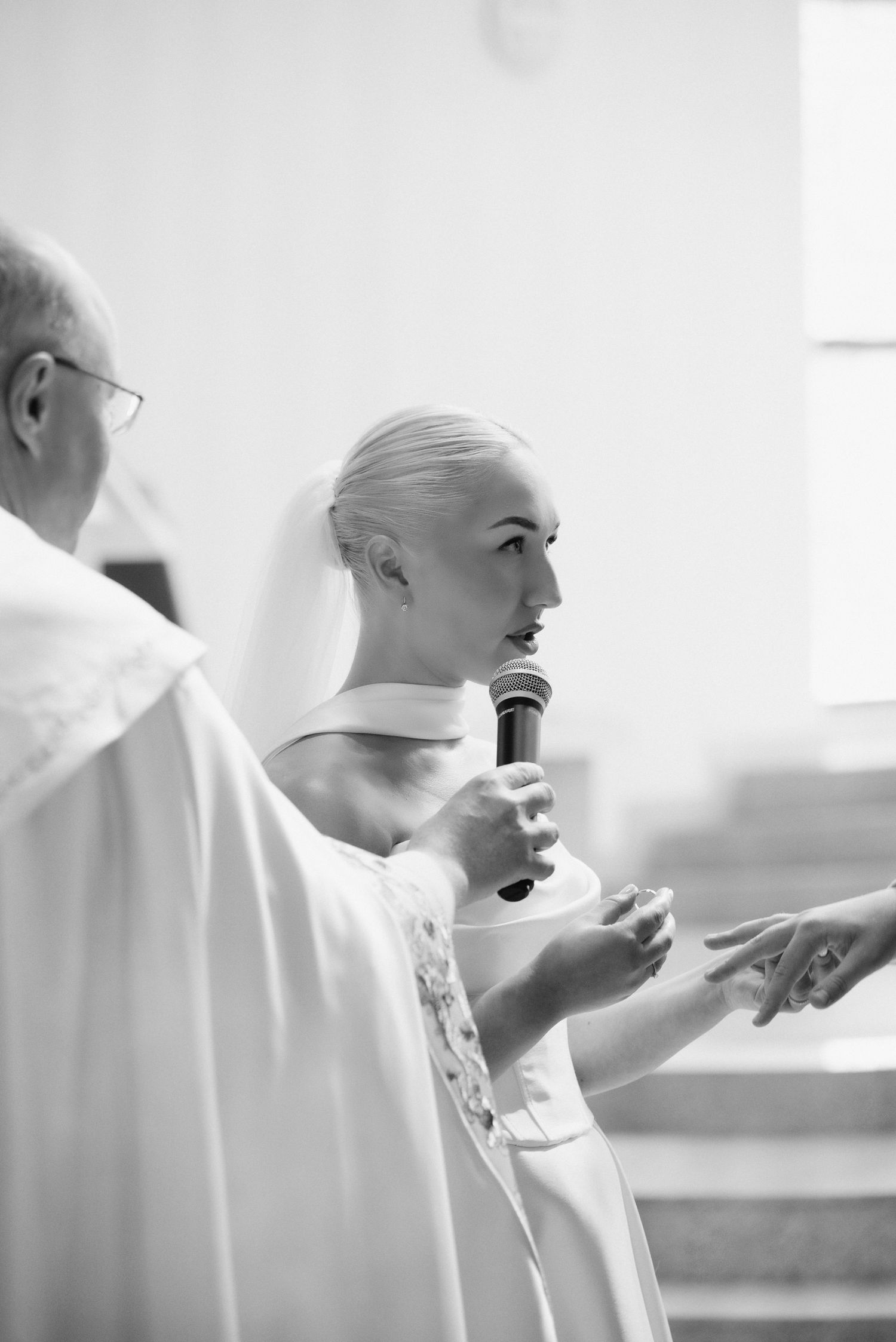 Black and white photo of the bride speaking into a microphone during the wedding ceremony inside a church in Lithuania. Klaipėda.