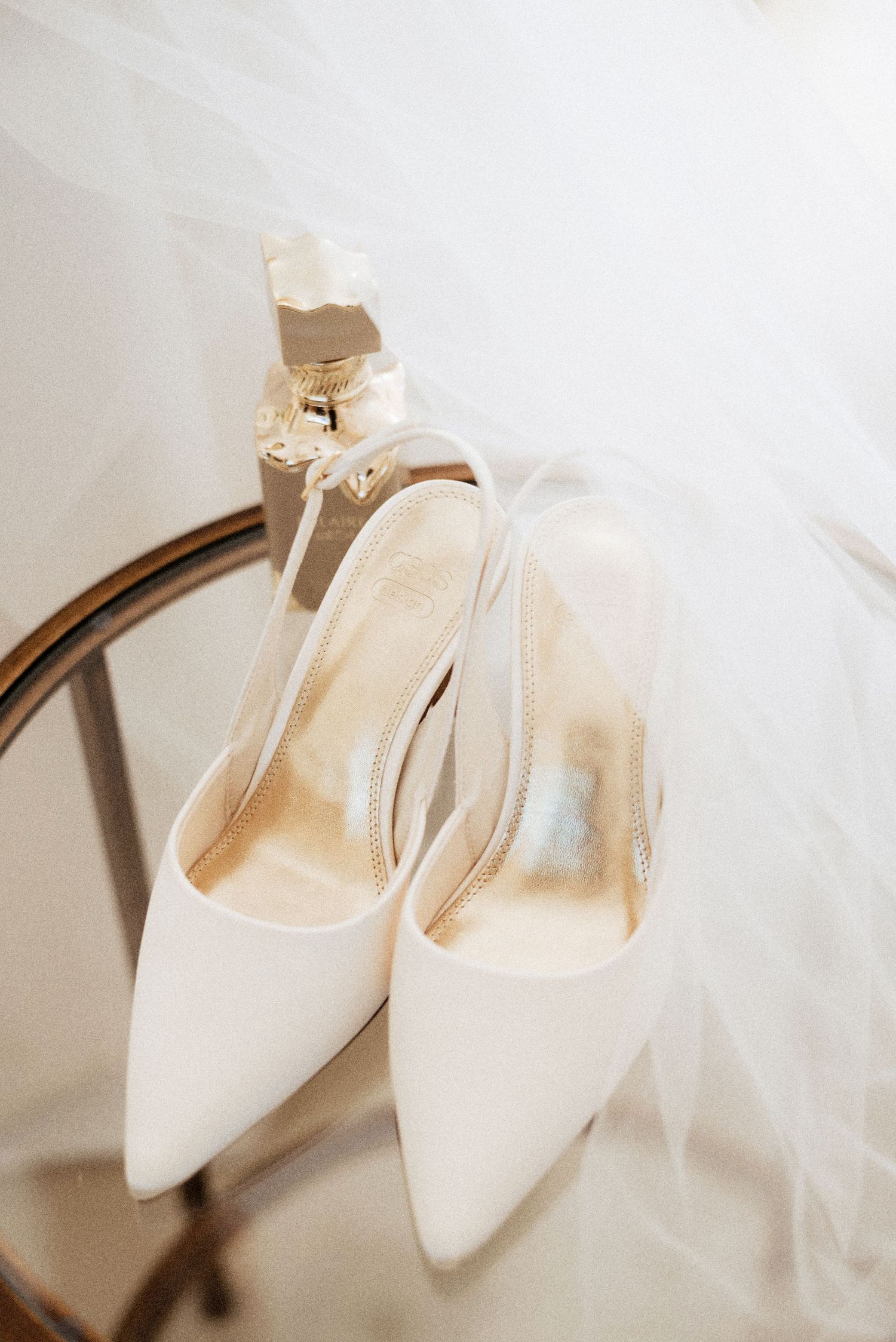 Elegant bridal shoes styled on soft white fabric with sunlight streaming in, captured as a fine art flat lay in Tuscany, Italy.