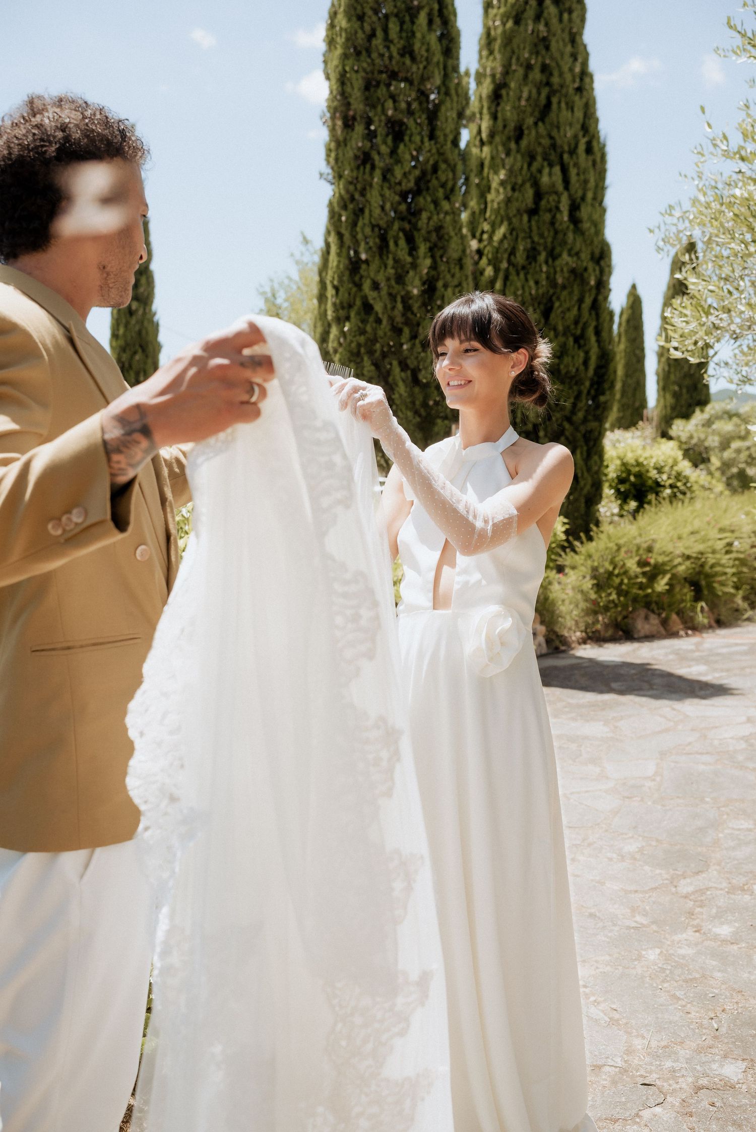 Groom walking with the bride along a Tuscan garden path, helping lift her dress as they smile together.