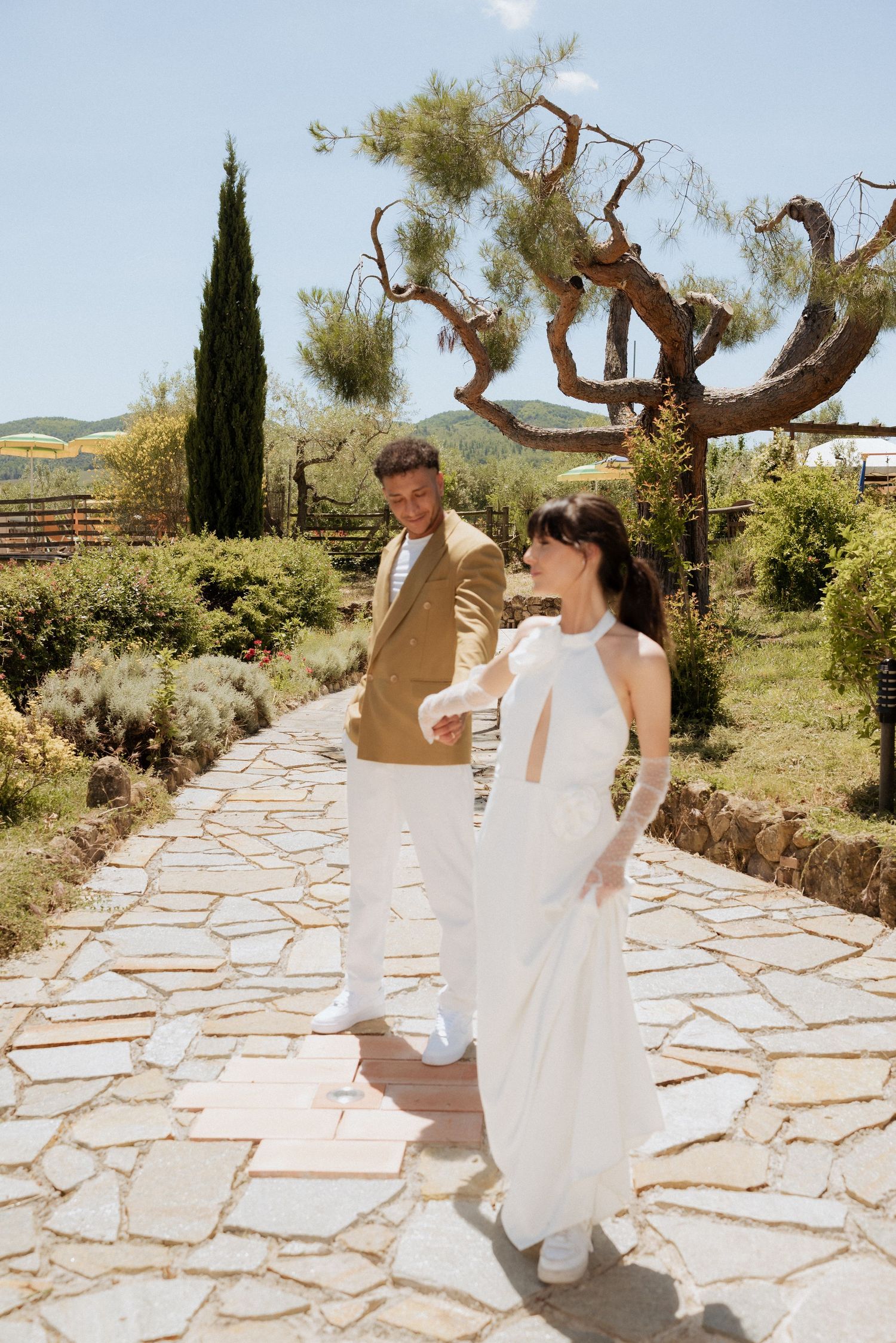 Bride walking down stone steps through a Tuscan garden, holding her bouquet and smiling softly.