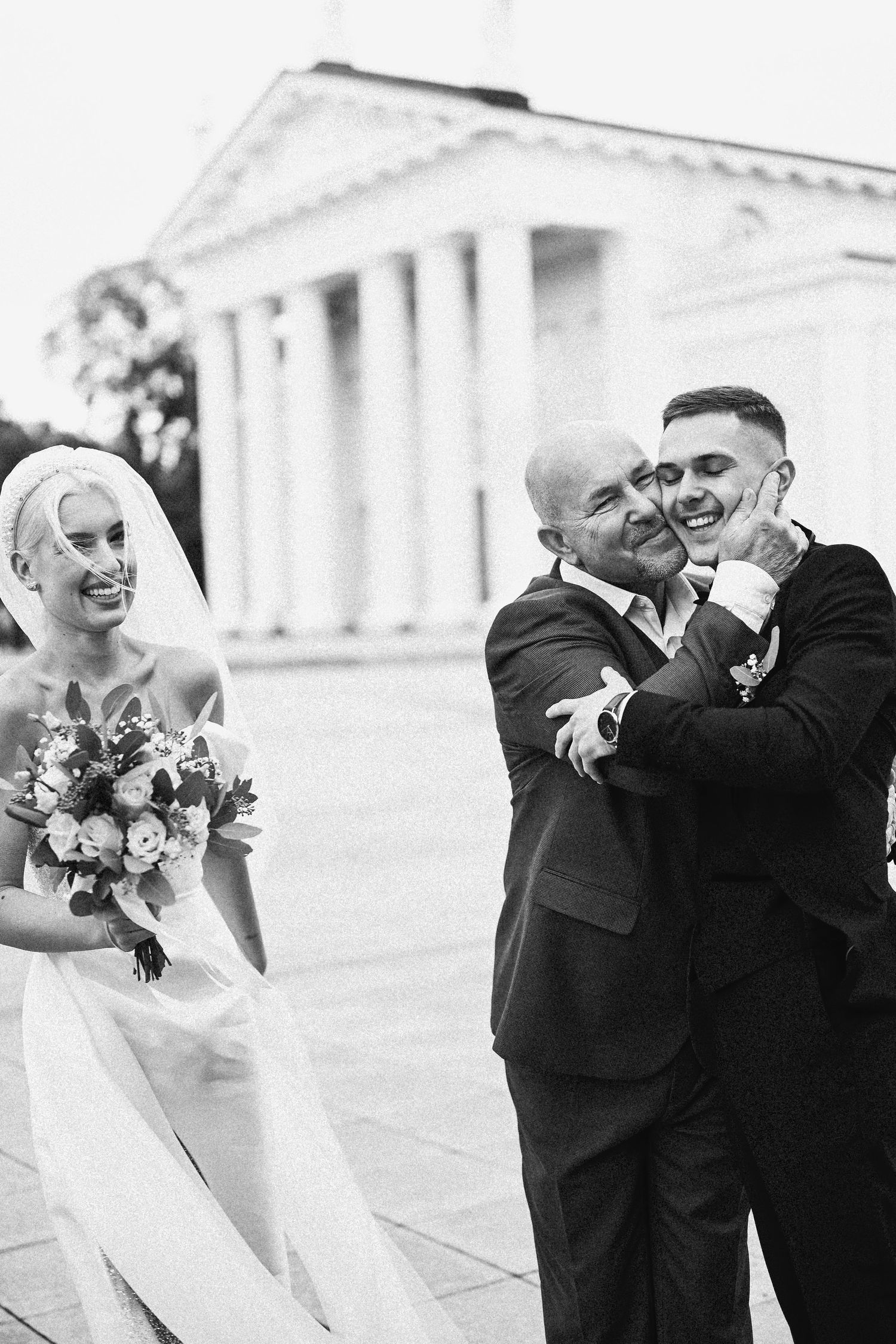 Candid moment of the bride, her father, and the groom sharing a warm greeting outside the venue, full of emotion and connection.