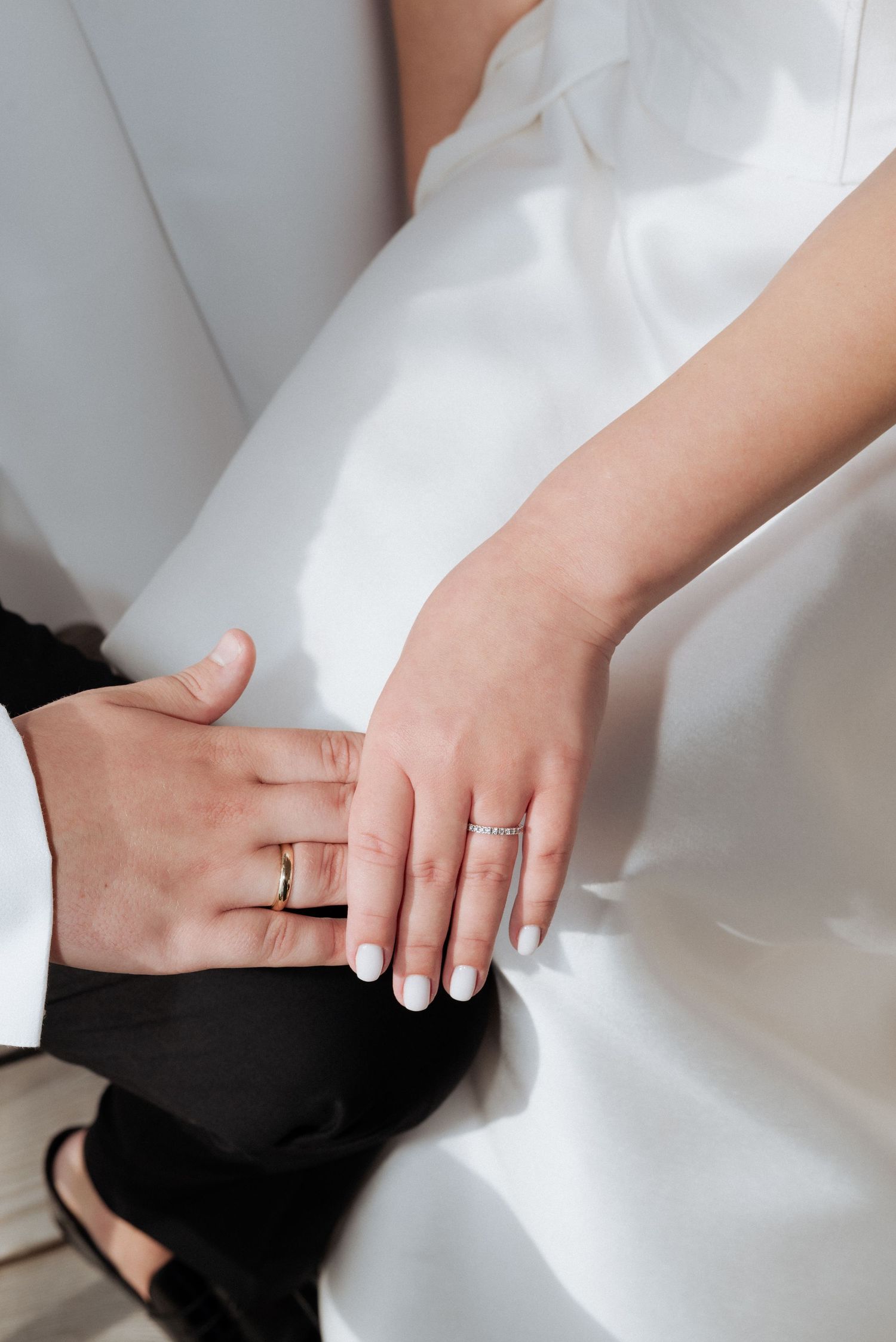 Close-up of the couple’s hands gently resting on the bride’s dress, highlighting wedding rings and connection.