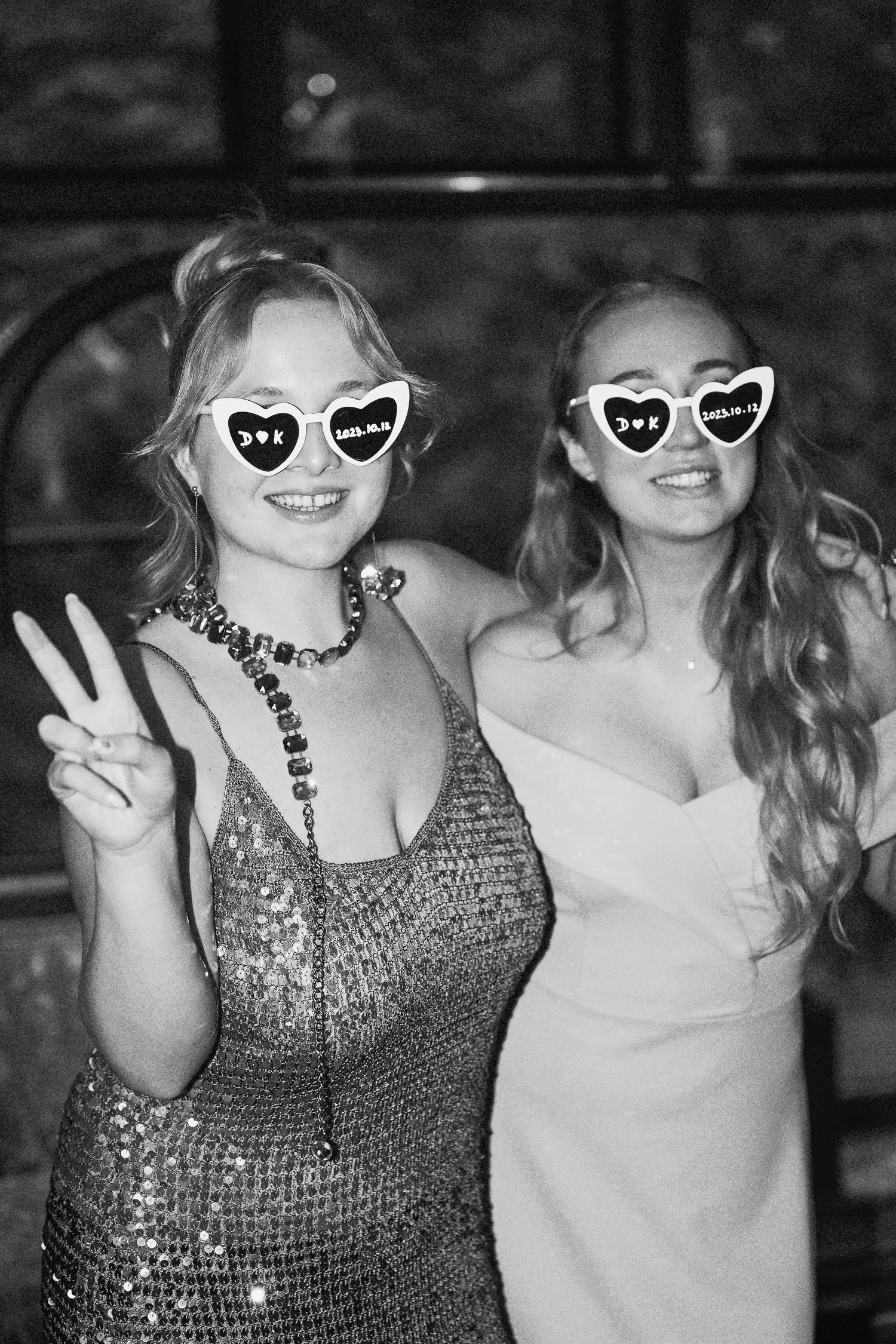 Two women laughing and hugging during an evening wedding celebration, caught on film.