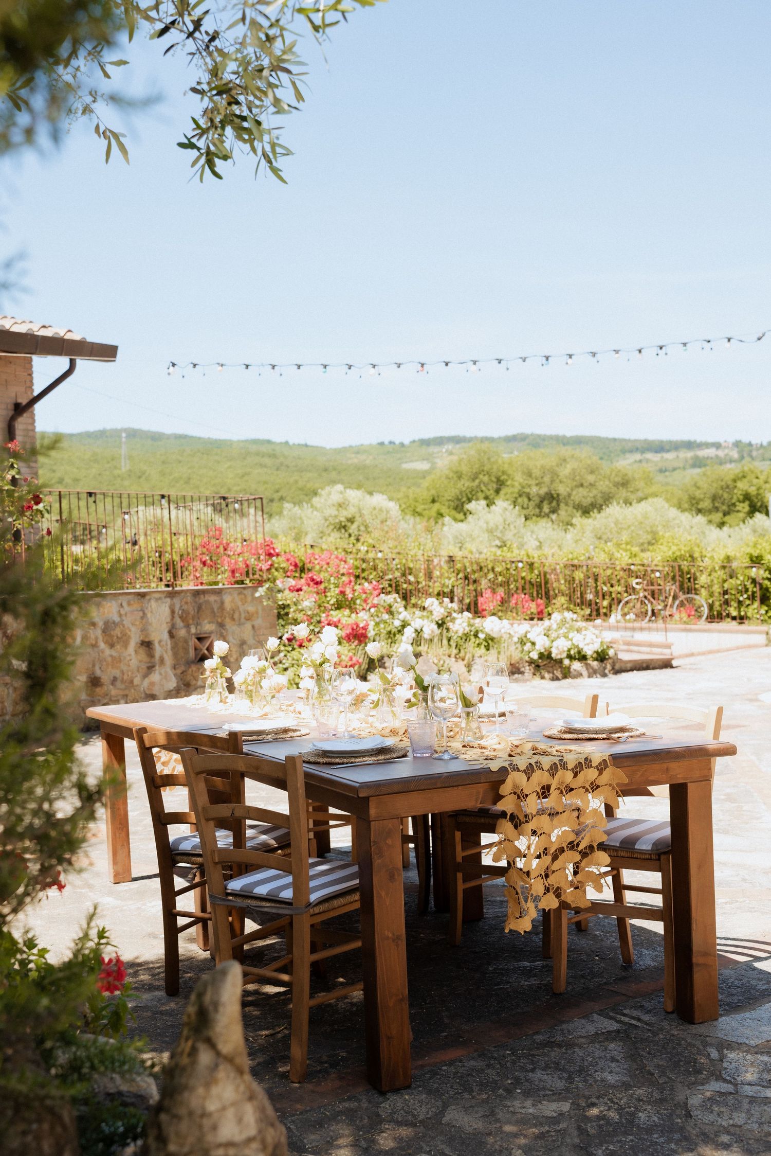 Outdoor Tuscan courtyard decorated for a wedding, with wooden pergola, floral details, and countryside views.