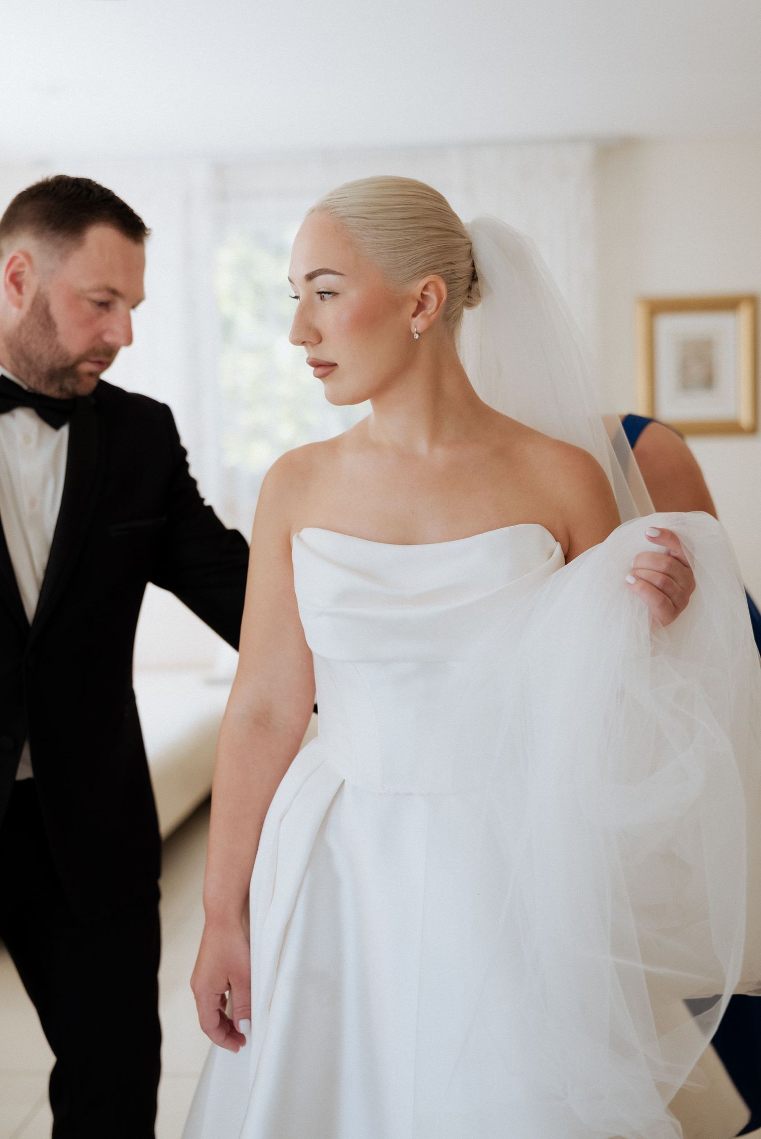 Bride’s father helping her with the wedding dress before the ceremony, captured in a heartfelt and tender indoor moment when getting ready.