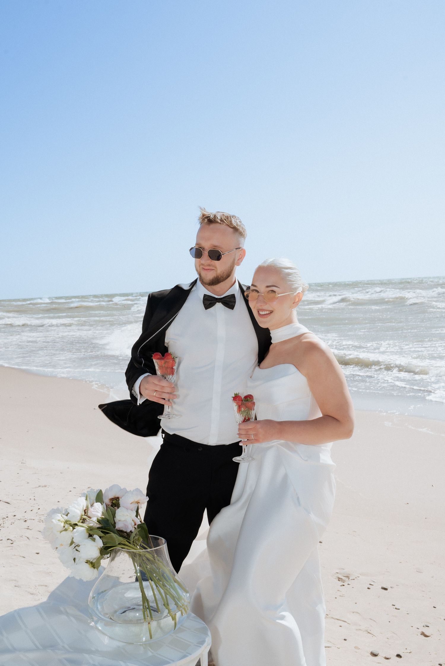 Newlyweds laughing together on a sandy beach with the ocean behind them, celebrating a destination wedding at seaside