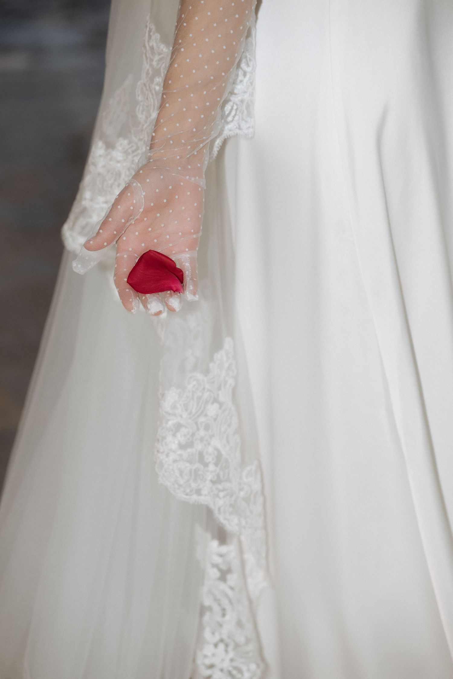 Close-up of the bride holding a red rose beside her wedding gown, captured in a quiet, emotional moment in Tuscany.
