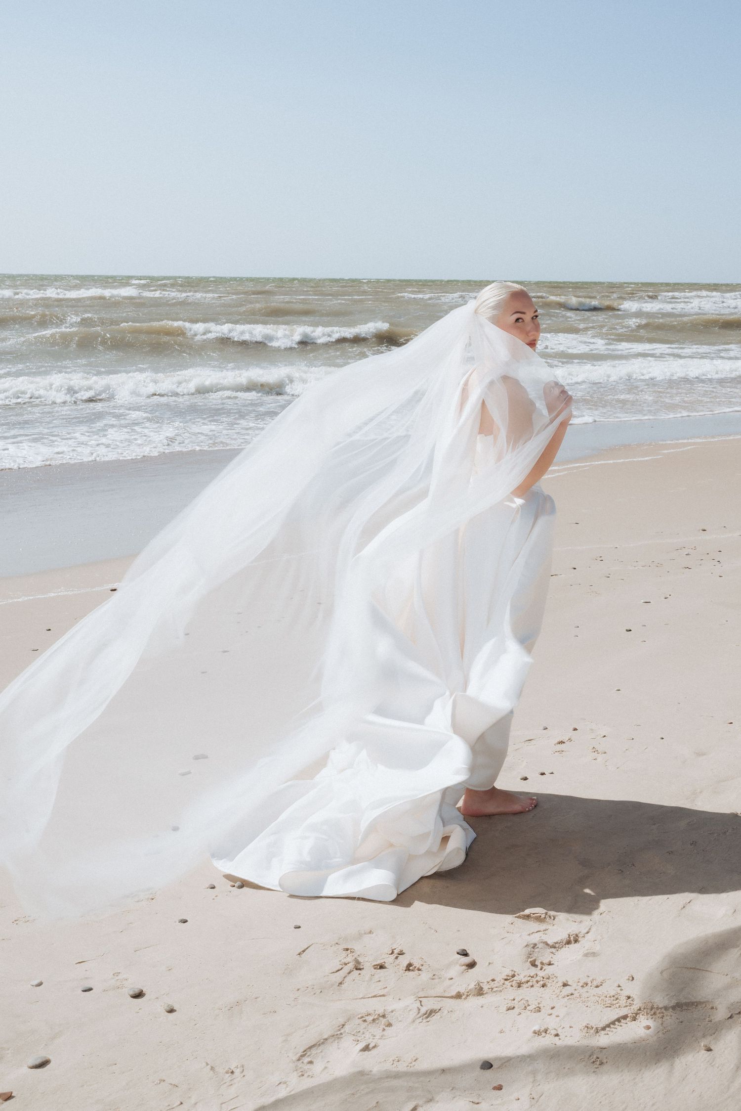 Bride walking barefoot along the beach in her flowing dress, with the sea view stretching behind her.