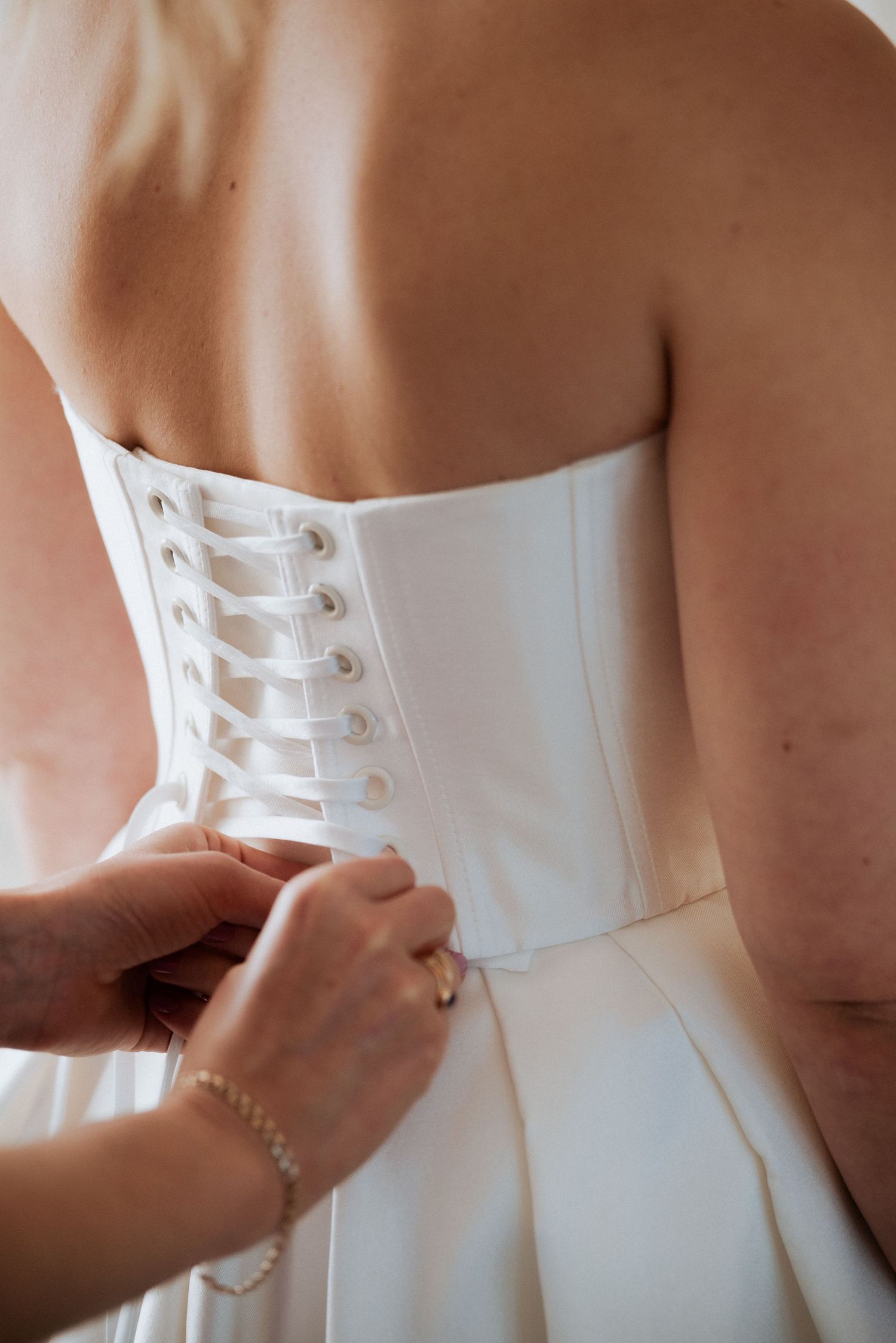 Close-up of hands buttoning the back of the bride’s dress, capturing an elegant pre-ceremony moment.