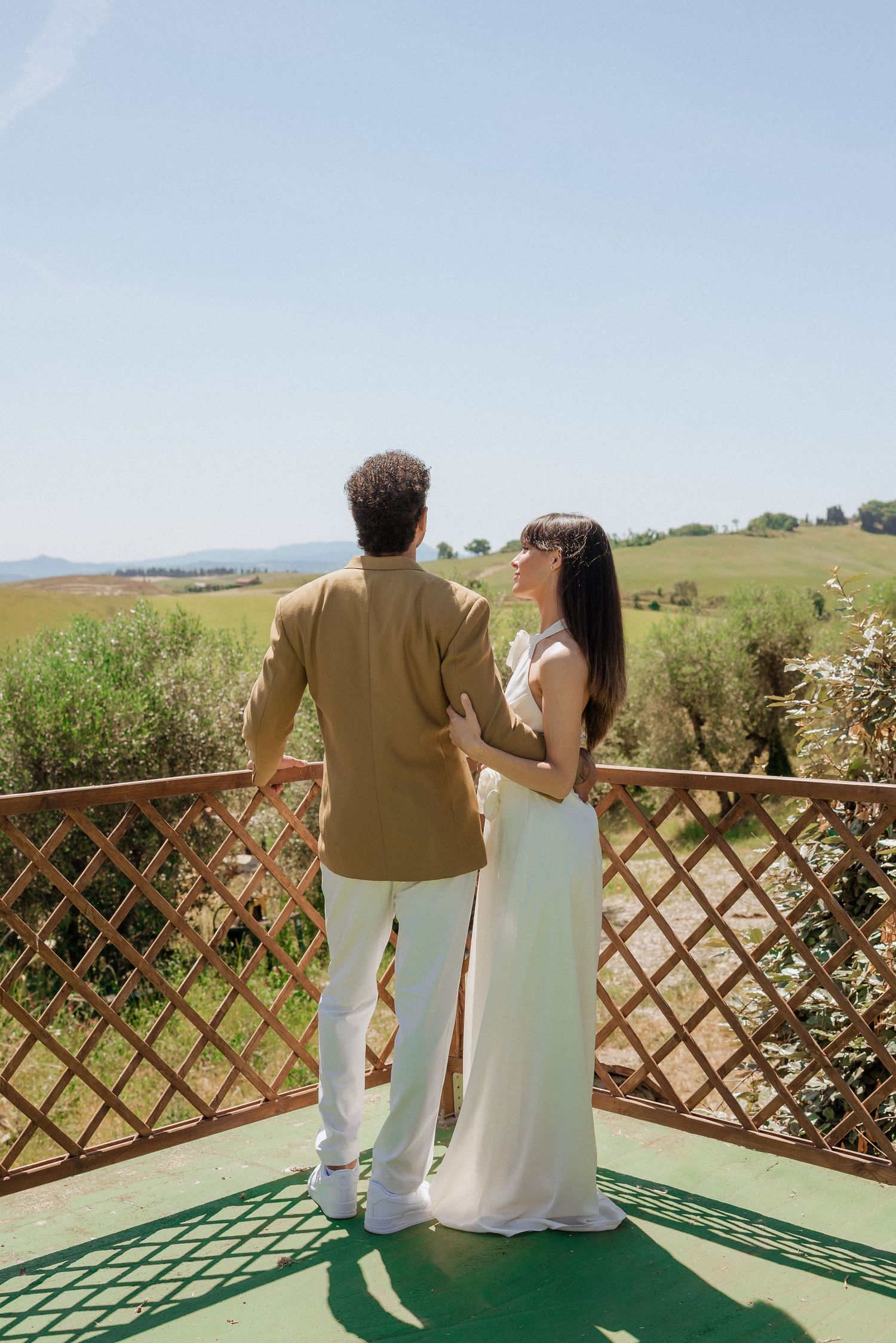Bride and groom standing together on a scenic terrace, enjoying a calm moment with countryside views behind them in Tuscany