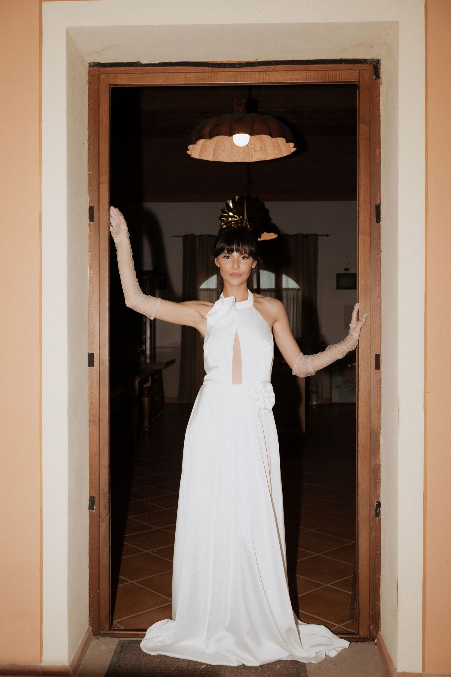 Bride standing in a doorway with her arms raised, wearing a fitted gown and looking confidently ahead.
