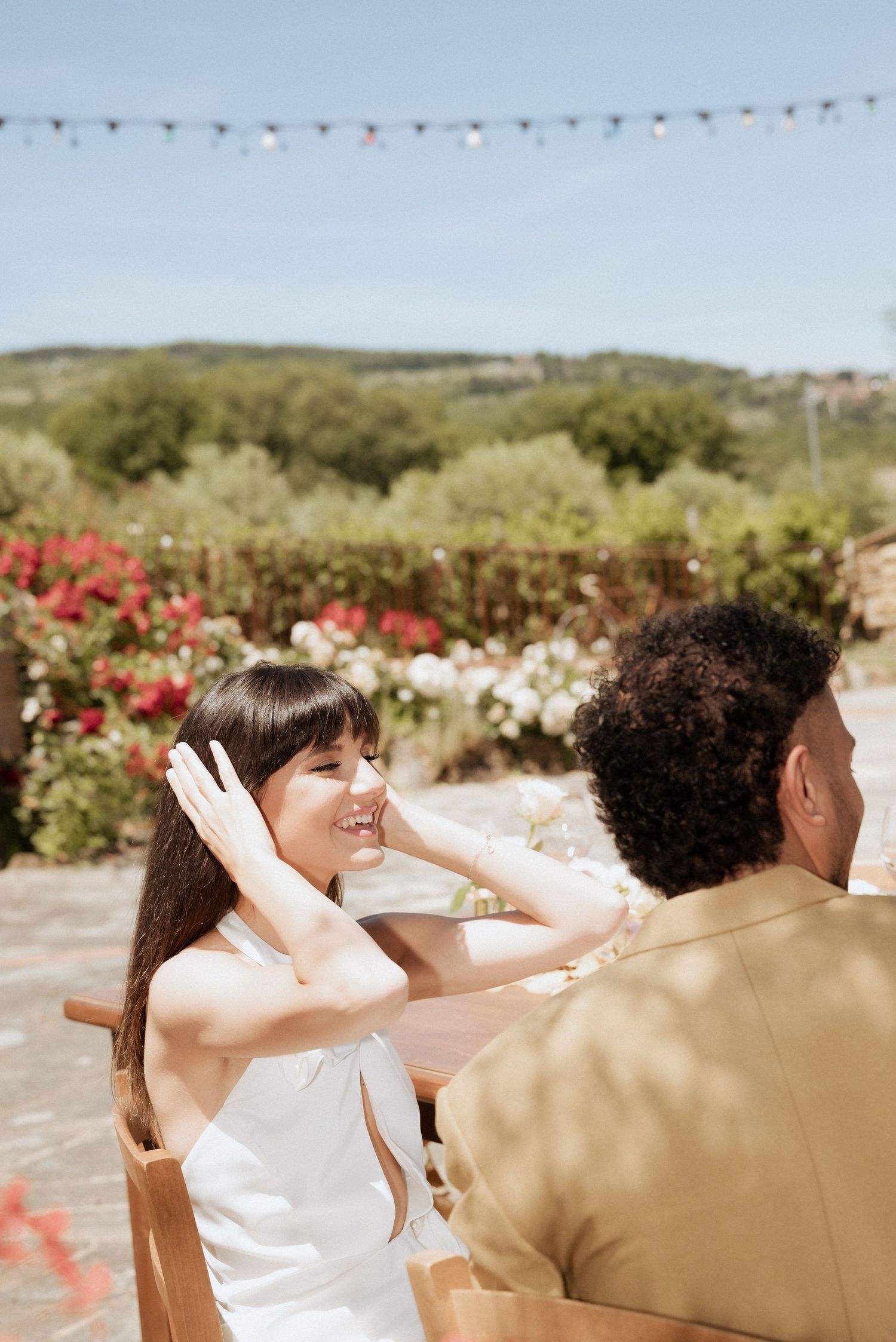 Bride and groom talking outdoors in front of a scenic Tuscan landscape, surrounded by warm sunlight and countryside views.