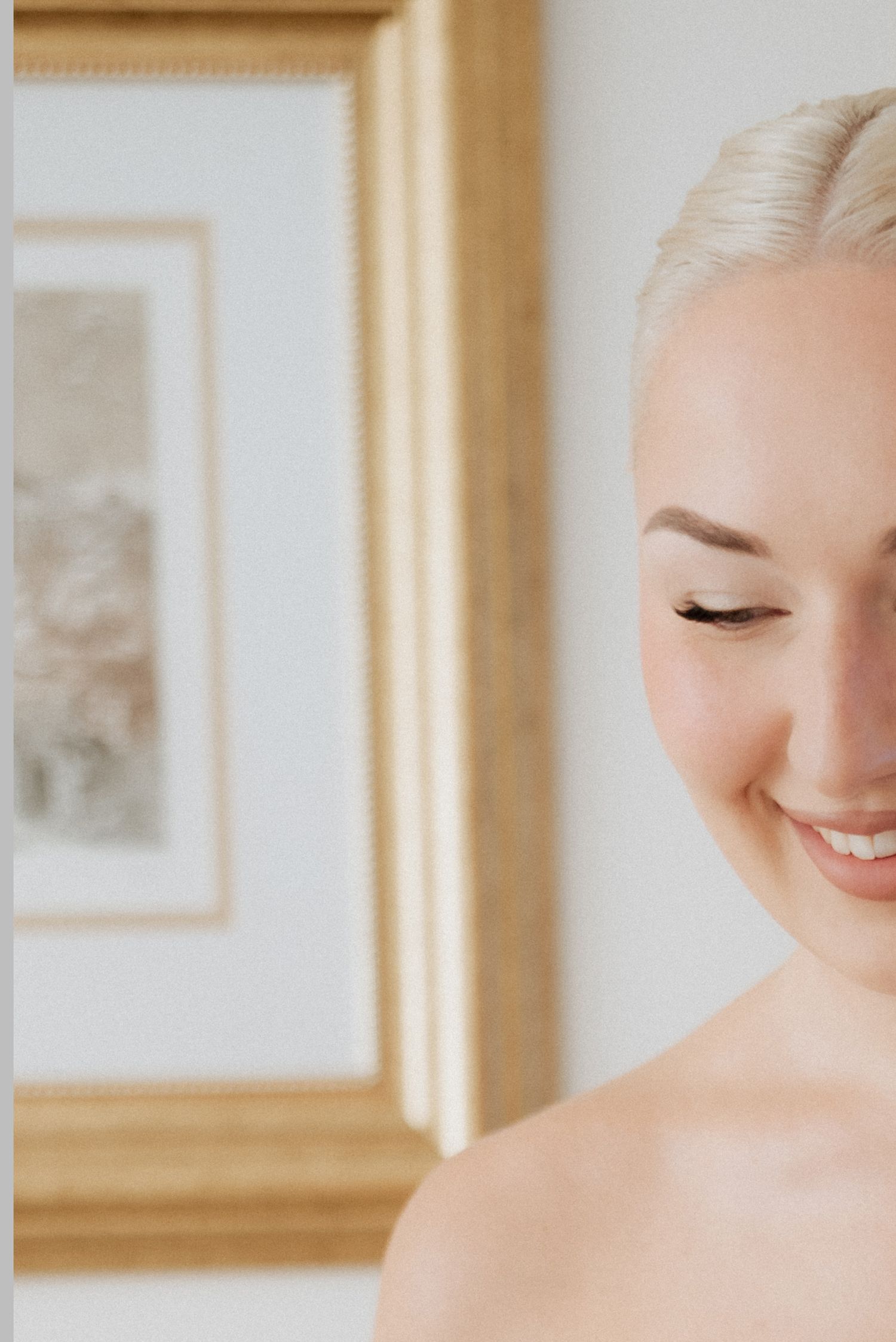 Soft bridal portrait with the bride smiling gently and eyes closed, framed in warm indoor light and minimalist elegance.