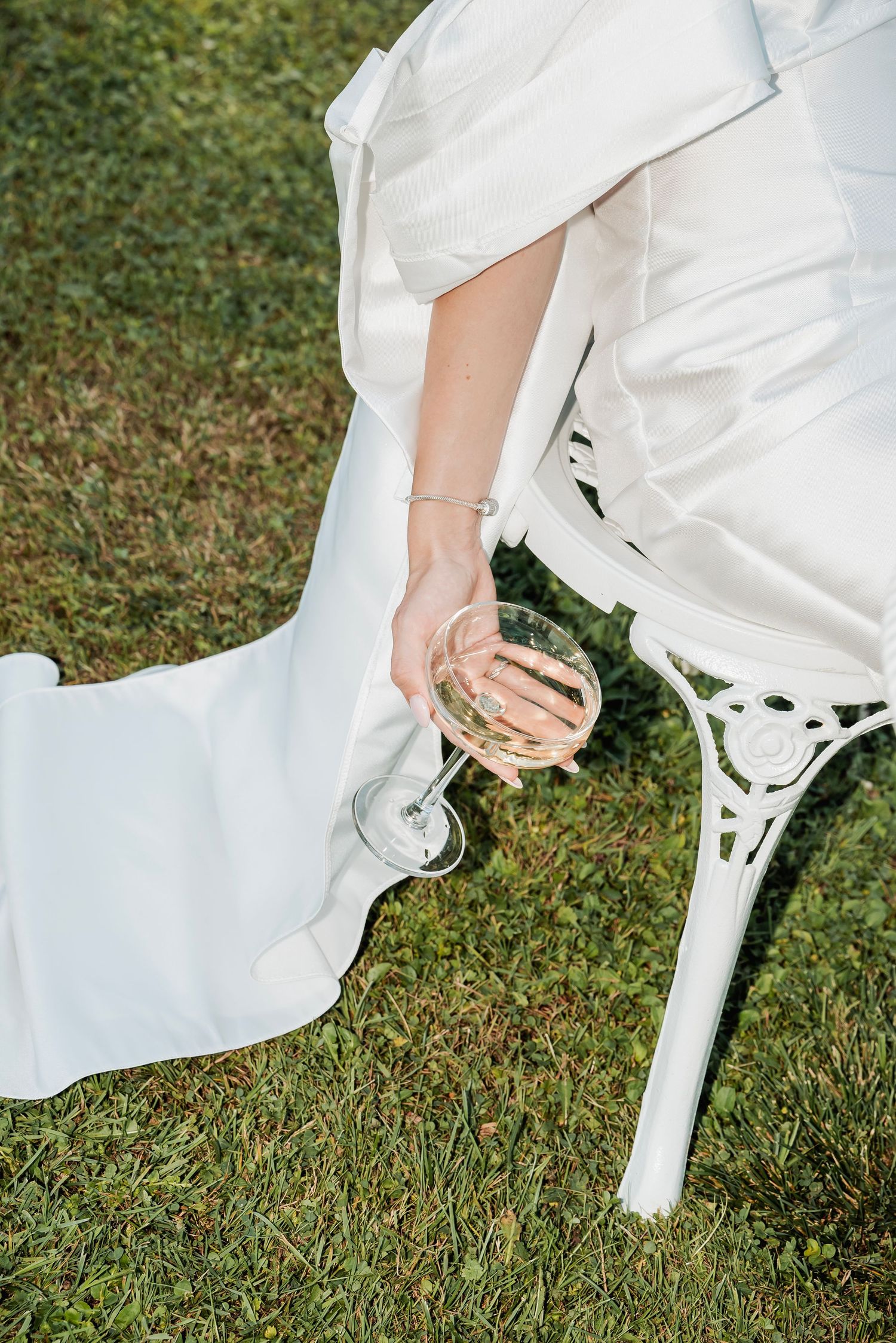 Bride sitting down outdoors, holding a glass in hand, with her heel slightly lifted and relaxed posture.