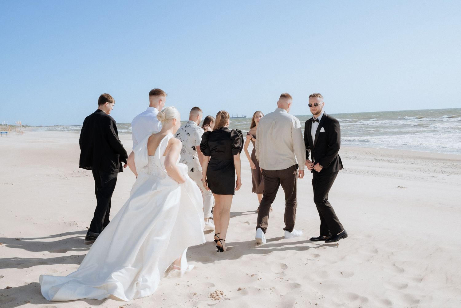 Bride walking along the beach with her wedding party, the sea in the background and wind blowing gently.