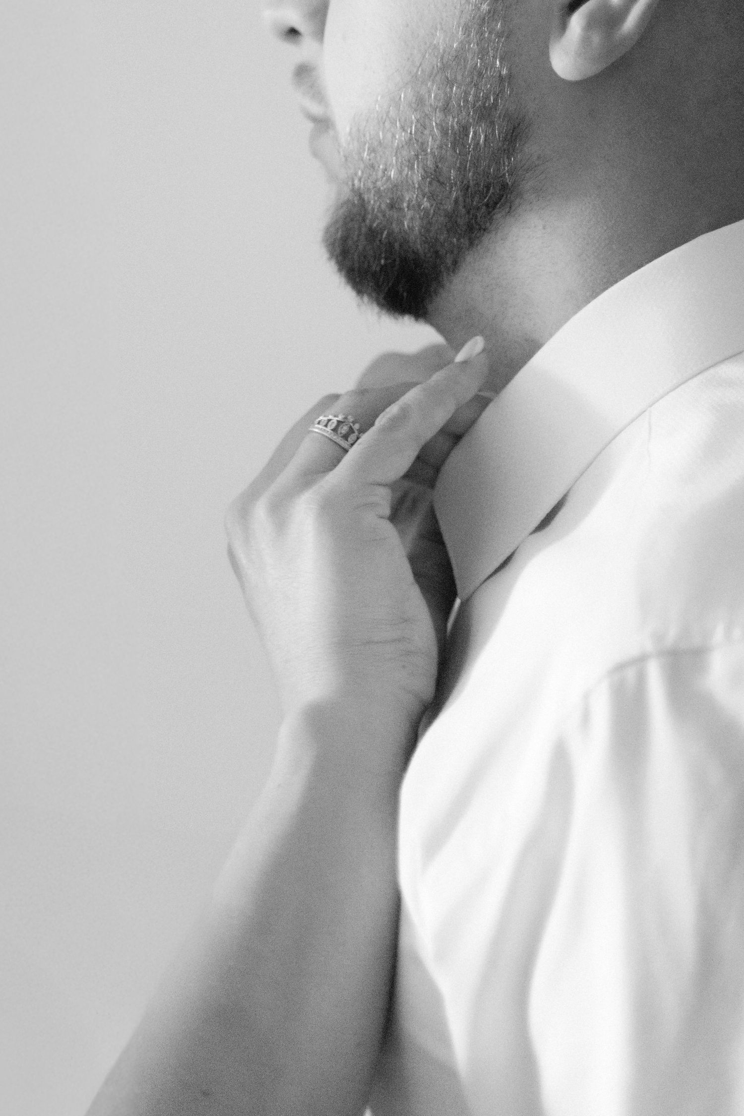 Groom adjusting his collar in a refined black and white close-up, showing anticipation before the ceremony.