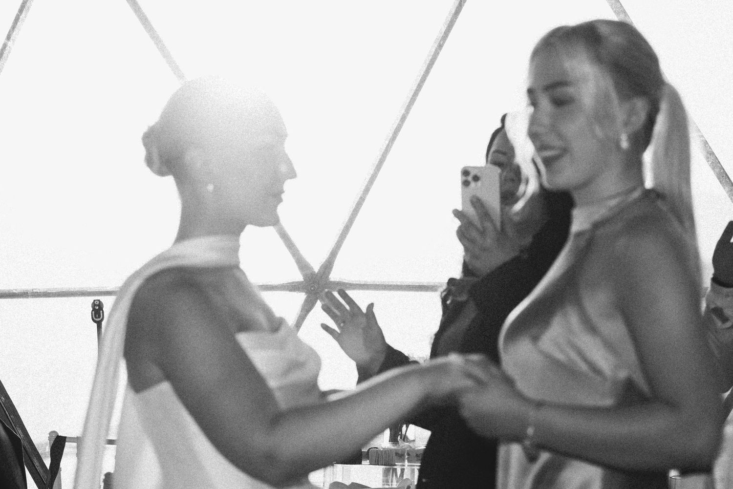Black and white photo of the bride smiling while greeting a guest during the wedding celebration under a transparent tent.