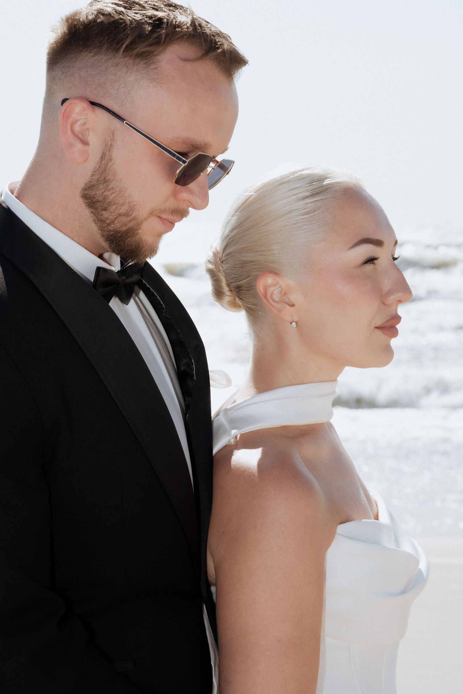 Close-up of the groom looking at the bride during a beachfront wedding, both dressed elegantly with the sea just behind them.