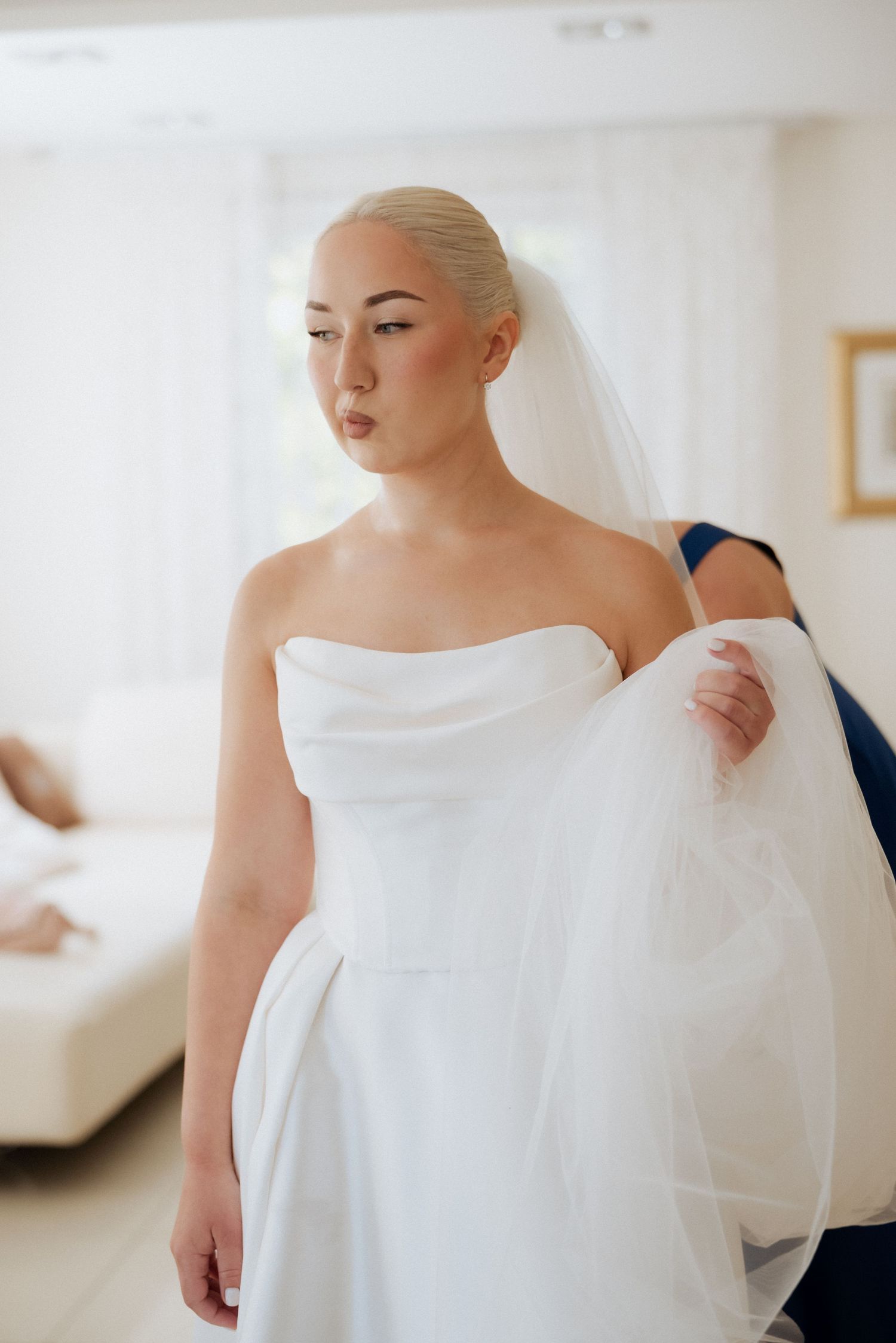 Bride looking down as she gently touches her dress, captured indoors in soft, warm light before the ceremony.