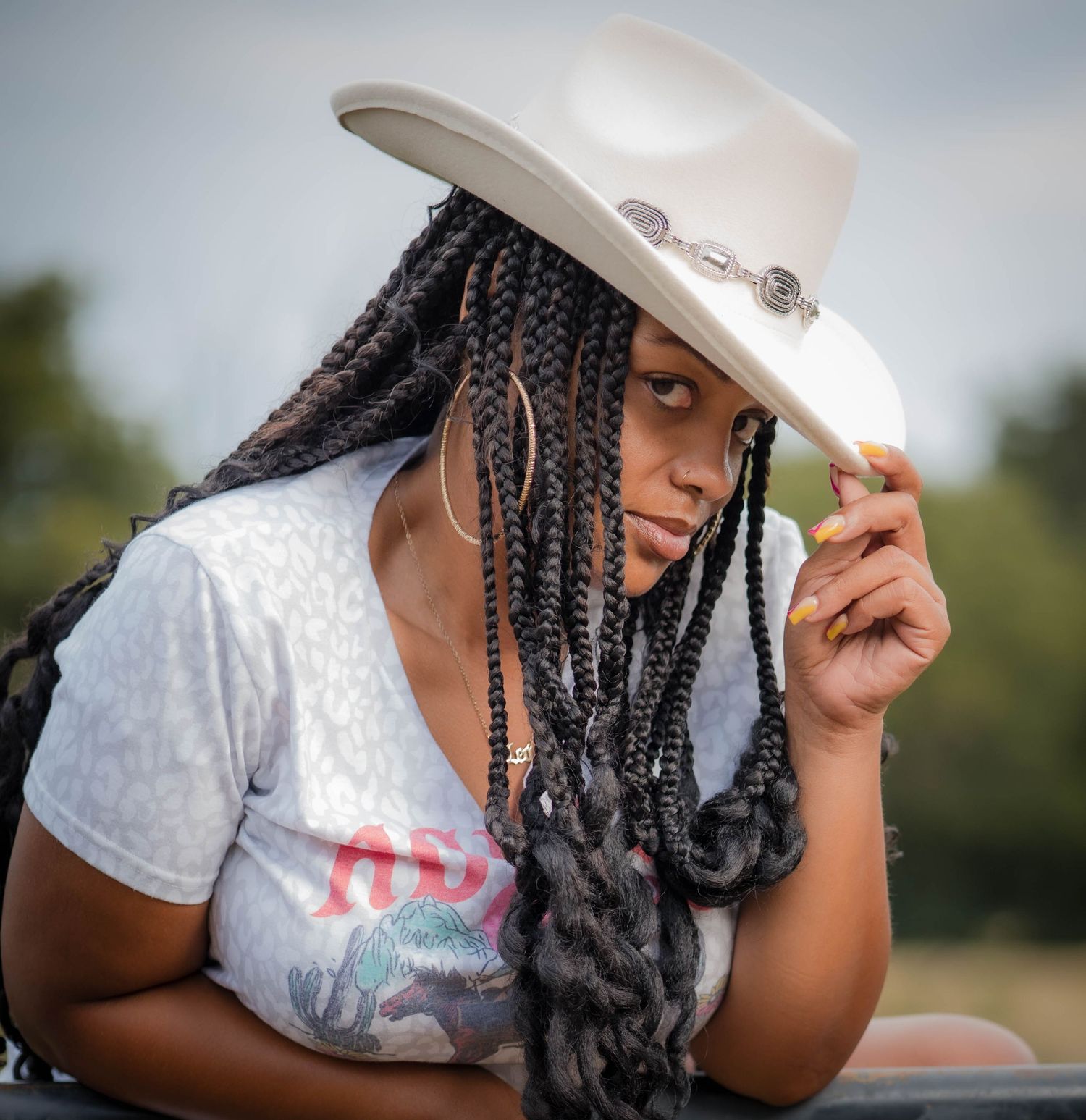 A casual portrait featuring a white cowboy hat and graphic t-shirt in natural lighting.