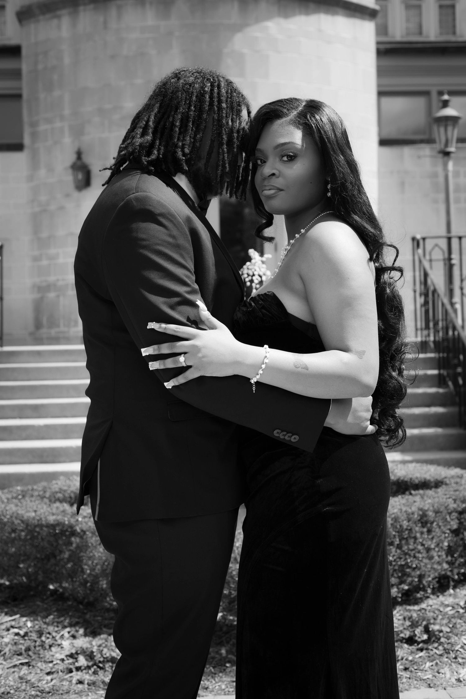A romantic black and white portrait of a couple in formal wear embracing outdoors.
