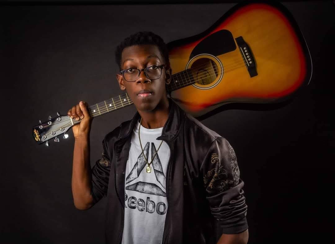 Musician poses with sunburst acoustic guitar against dark background.