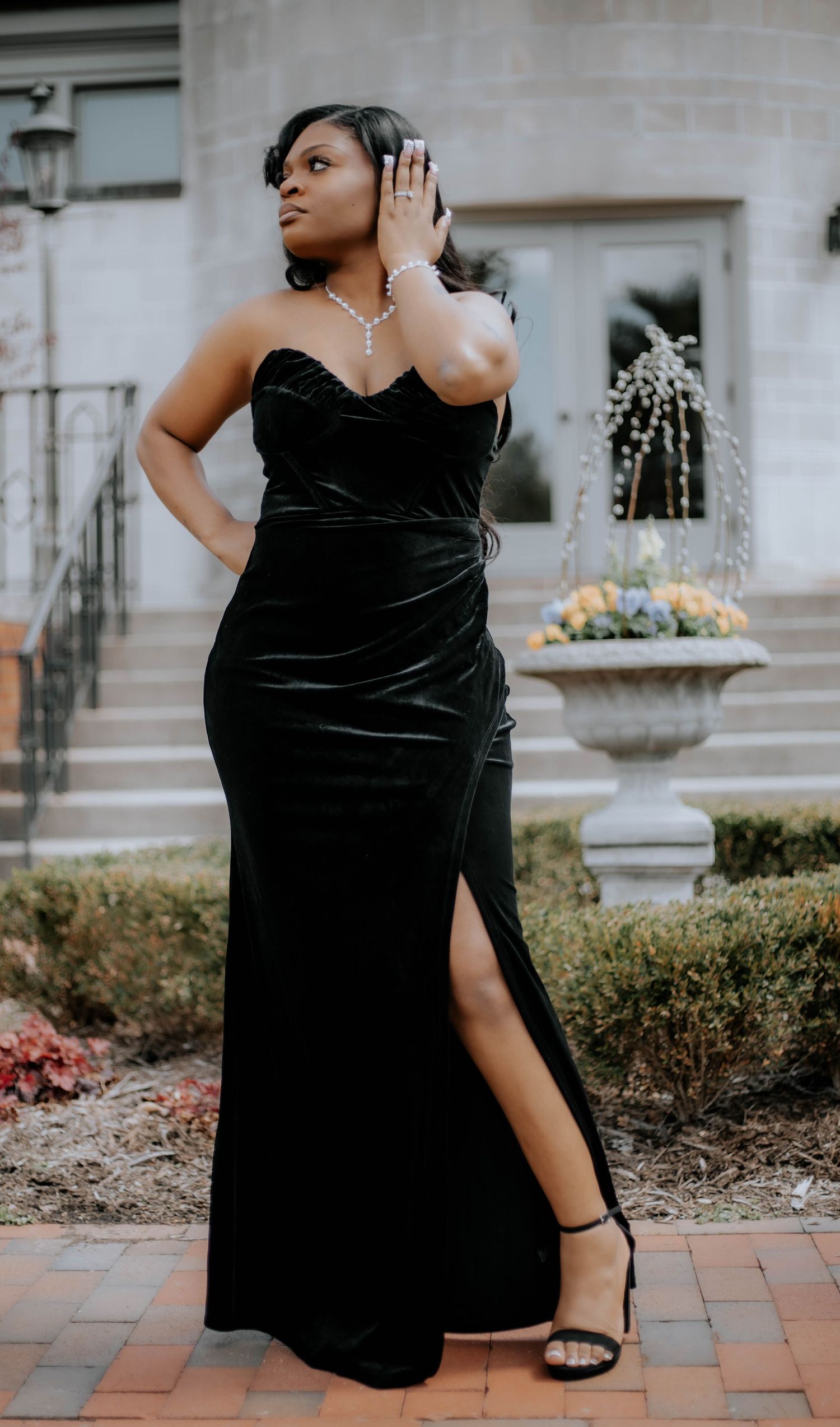 A portrait in a black velvet evening gown with side slit on brick pathway.