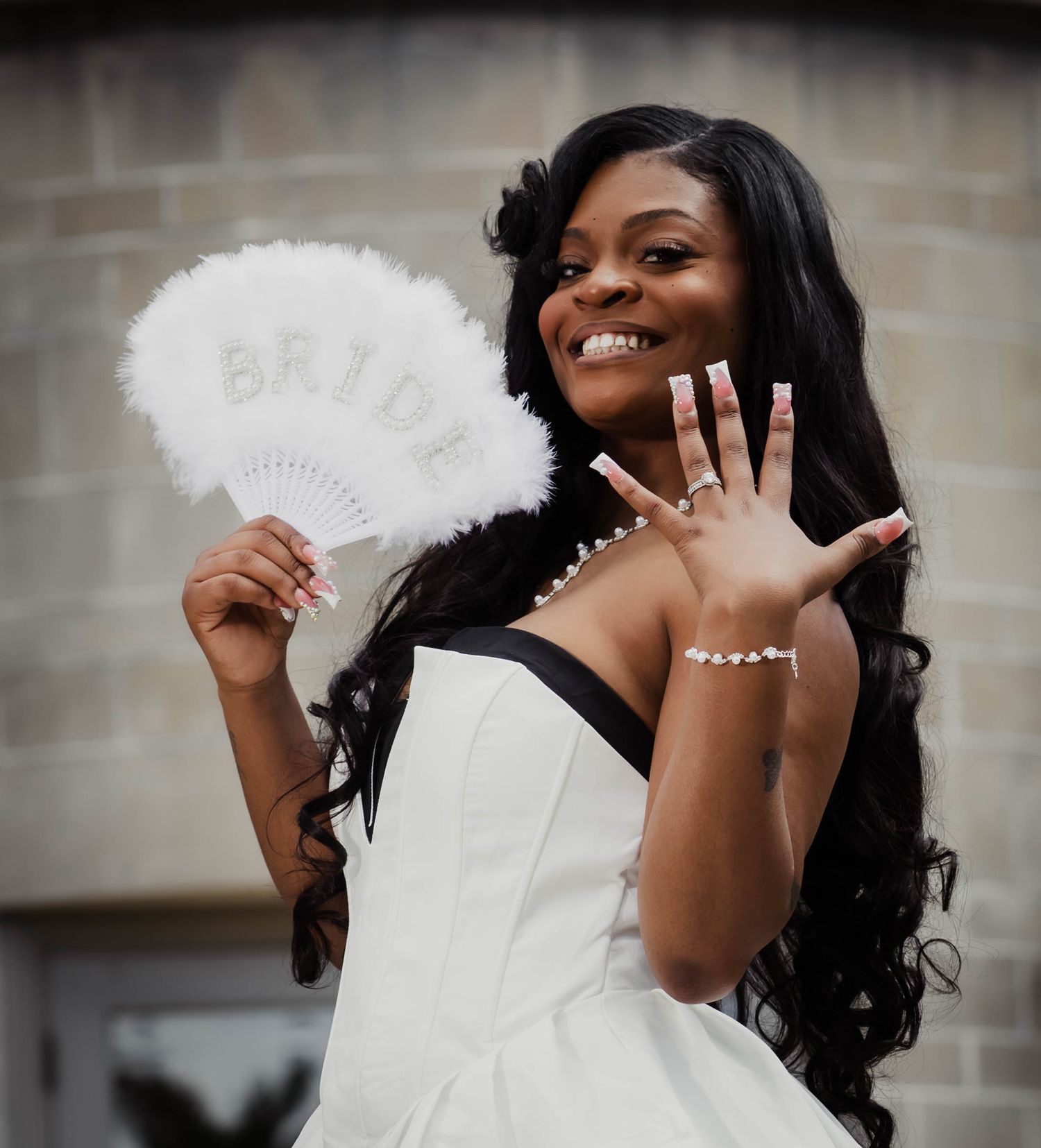 A joyful portrait showing off an engagement ring while holding a white feather fan.