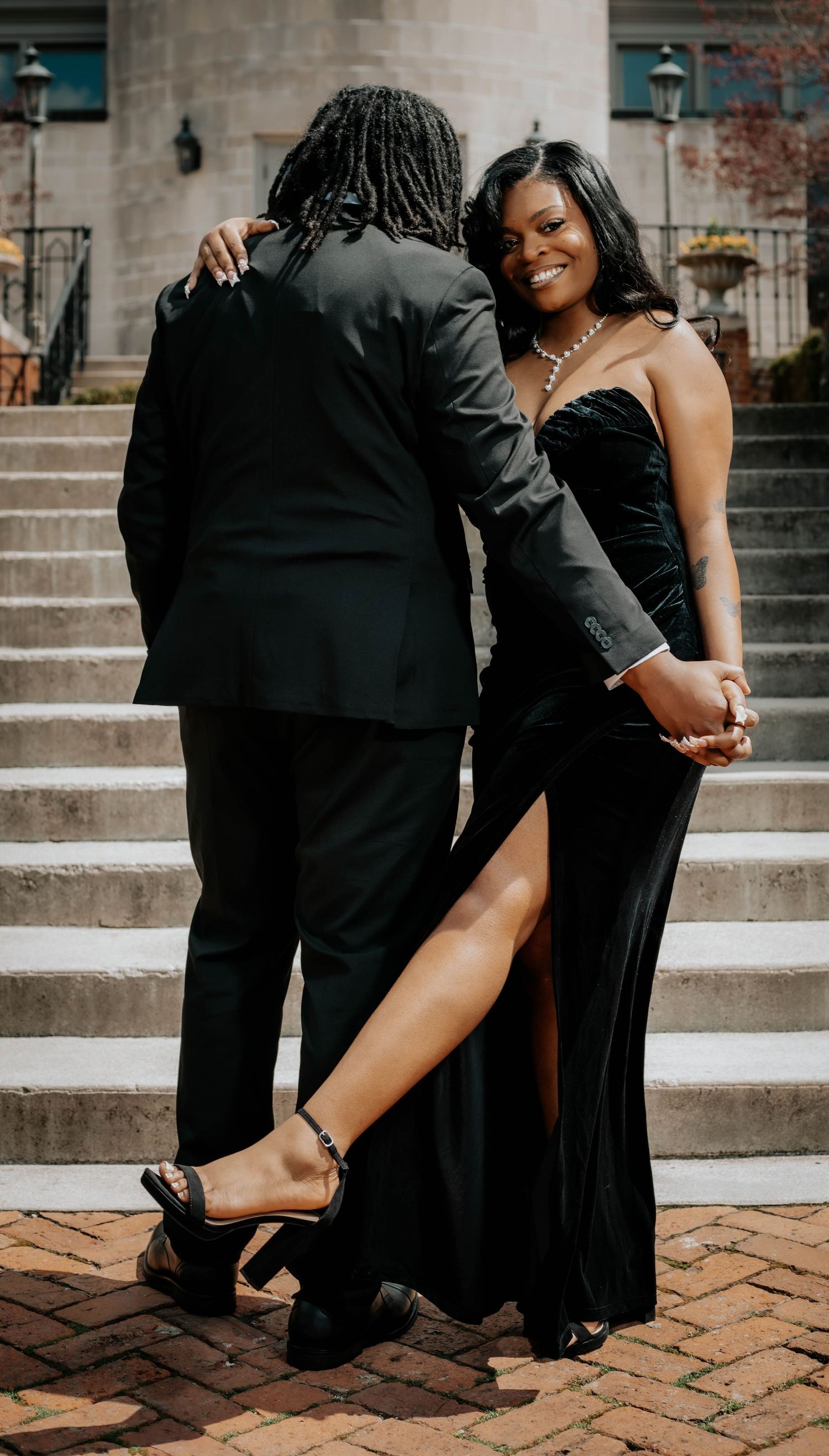 A couple in formal evening wear poses romantically on brick stairs.