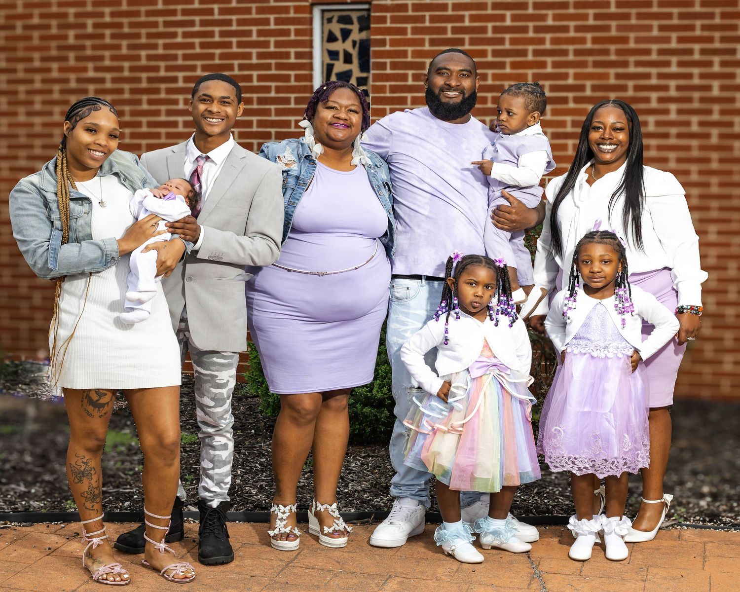 Large family group posing together outdoors in coordinated purple and white outfits for a special occasion photo.