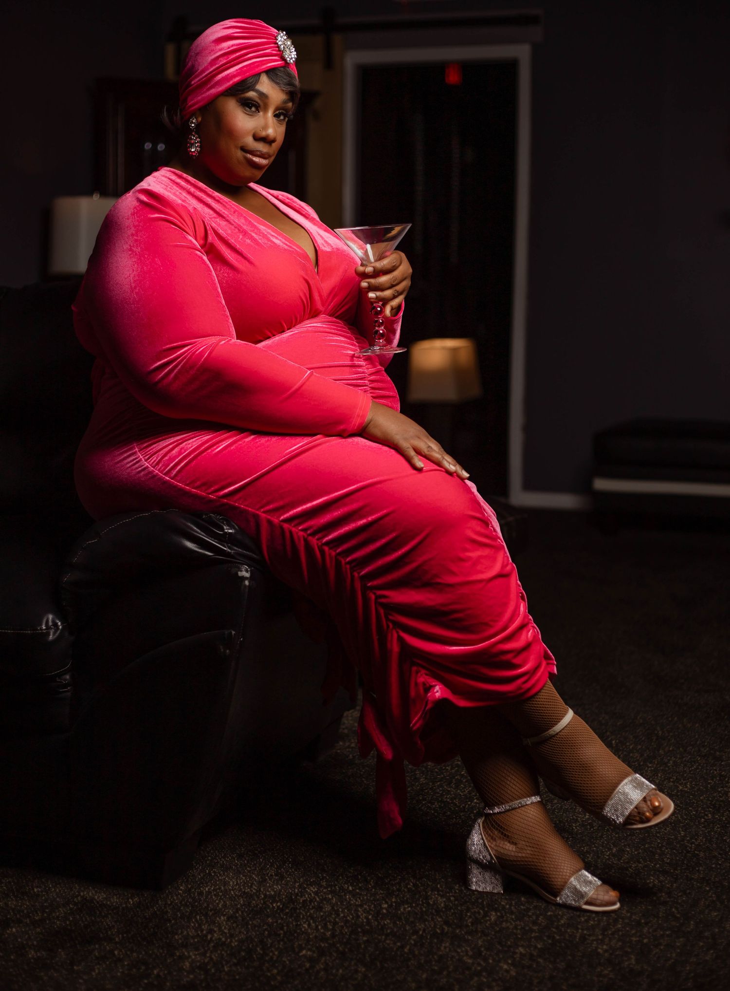 A person in vibrant pink attire sits in a dimly lit setting while looking at their mobile phone.