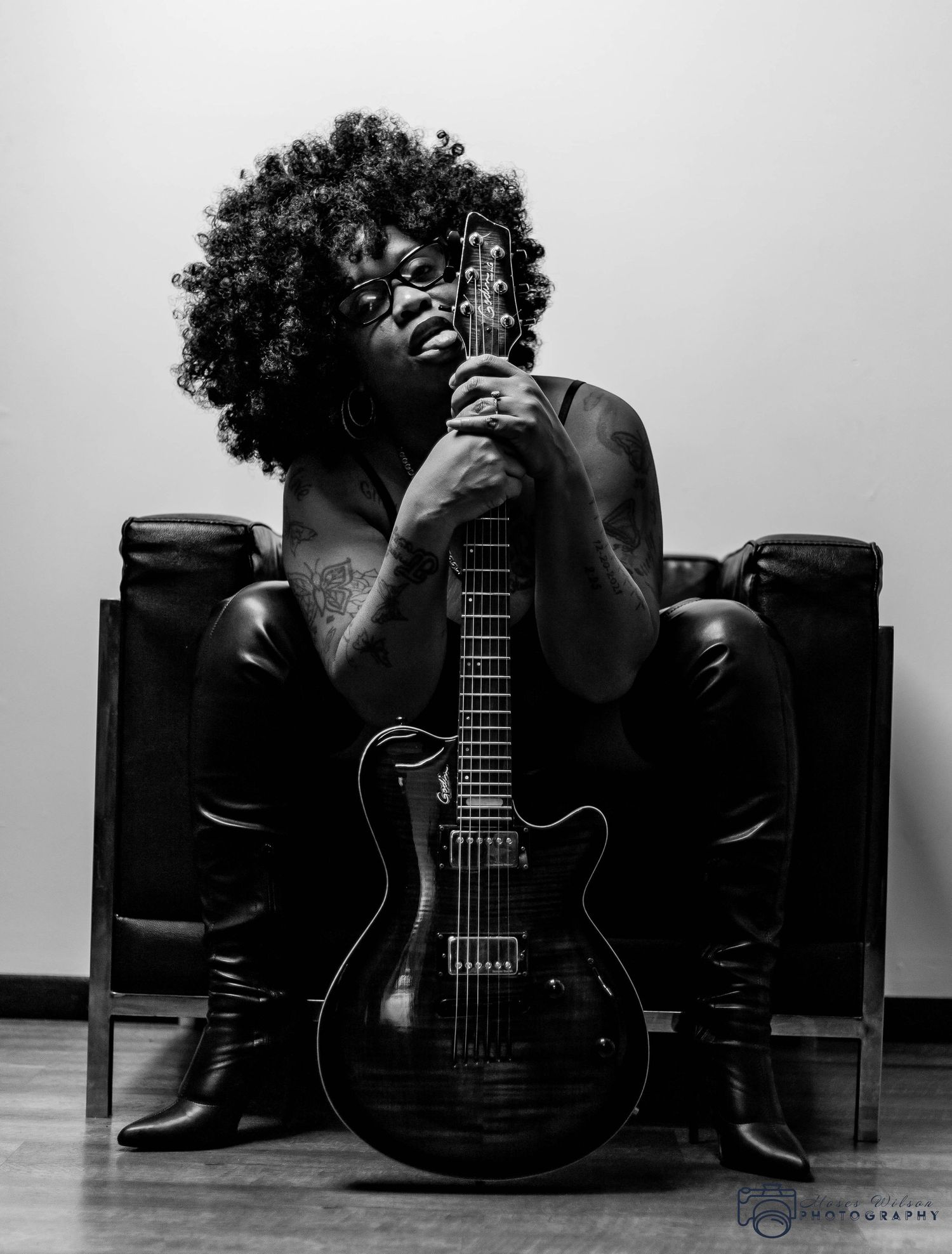 A black and white portrait shows a musician embracing an electric guitar while seated.