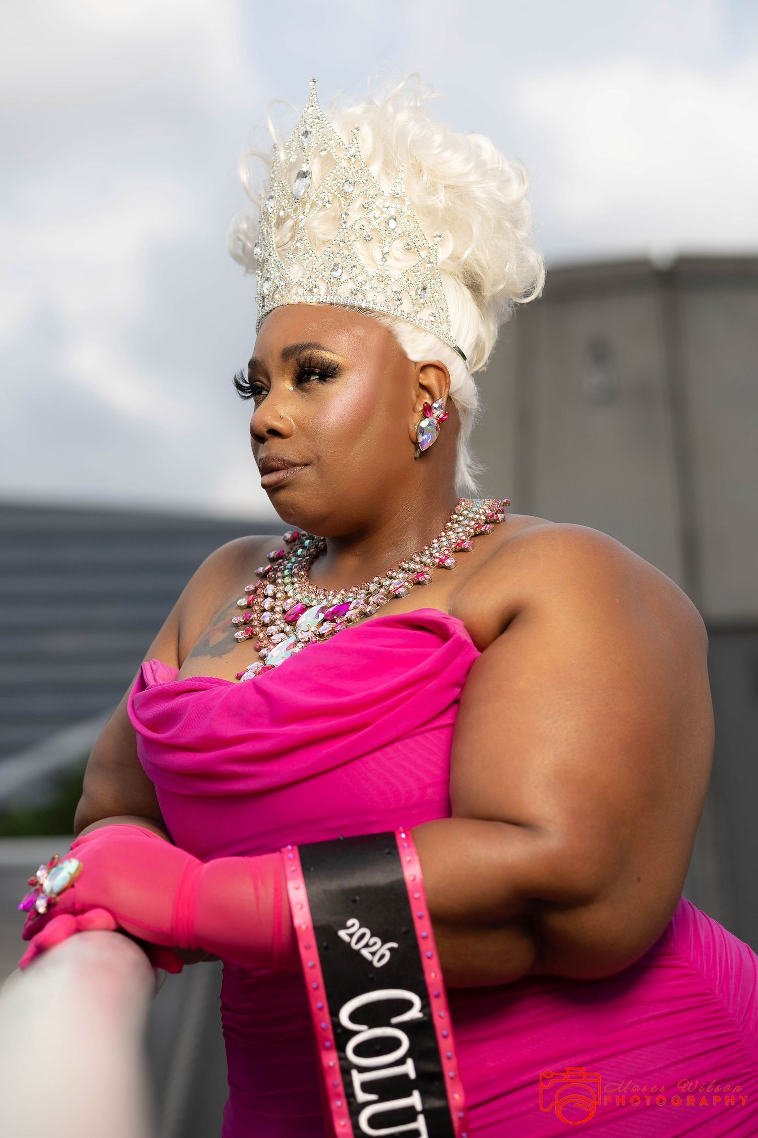 Woman in pink gown, jeweled crown, sash reading 2025 Columbus, poses confidently outdoors in pageant attire.