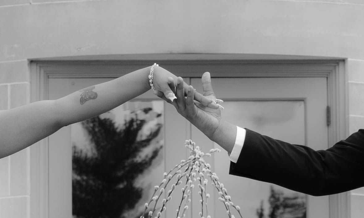 Black and white photo of hands toasting with champagne glasses against a garage door.