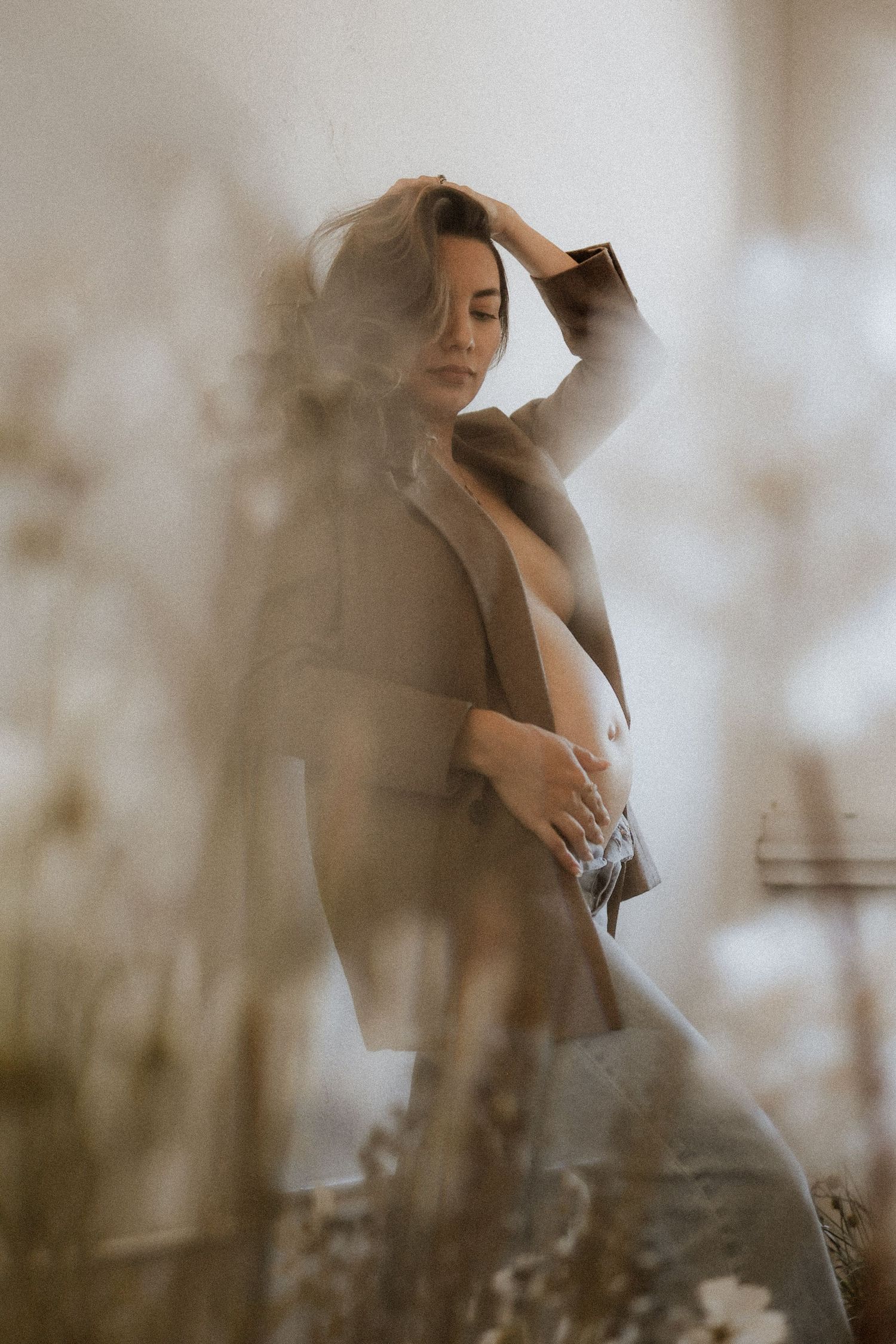 Dreamy portrait of someone in a beige coat posing with soft focus and ethereal lighting effects. maternity, baby bump, photoshoot