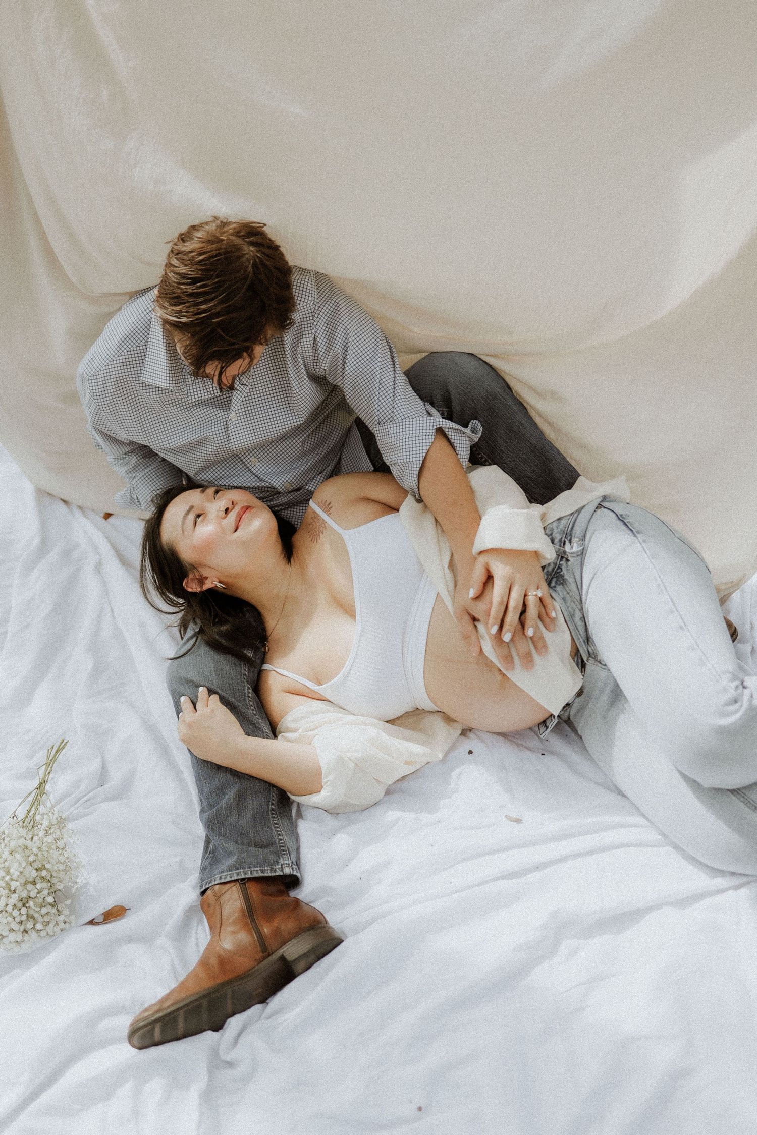Intimate maternity photoshoot series showing couple laying on white bedding in soft natural light. maternity, backyard, photoshoot